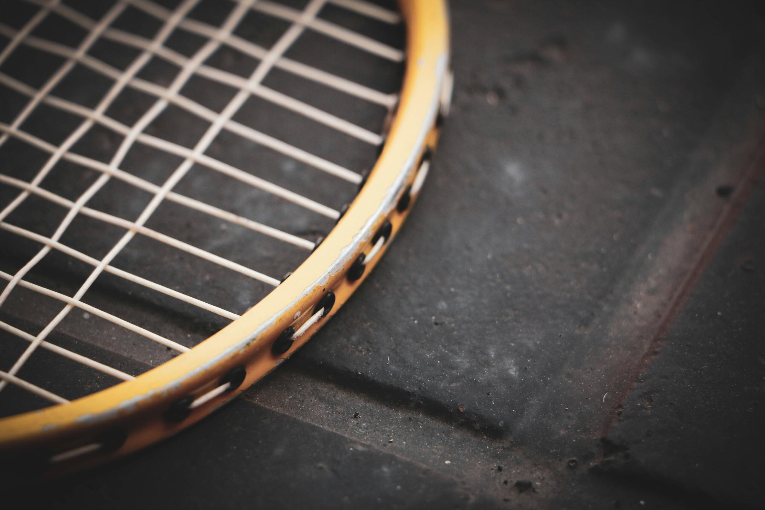 Close-up van de versleten gele rand en witte snaren van een tennisracket.