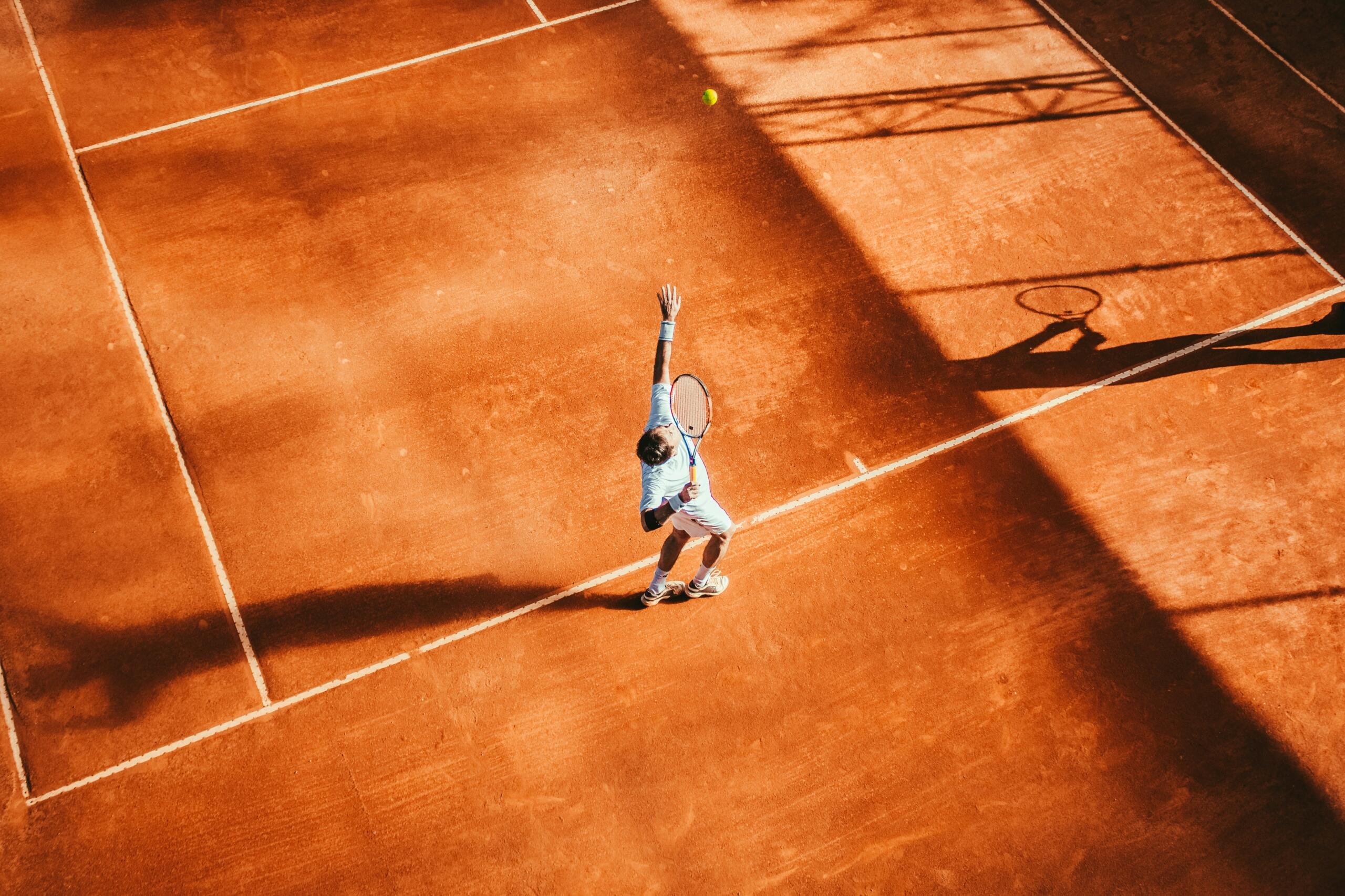 Een tennisser serveert op een gravelbaan, van bovenaf gefotografeerd.