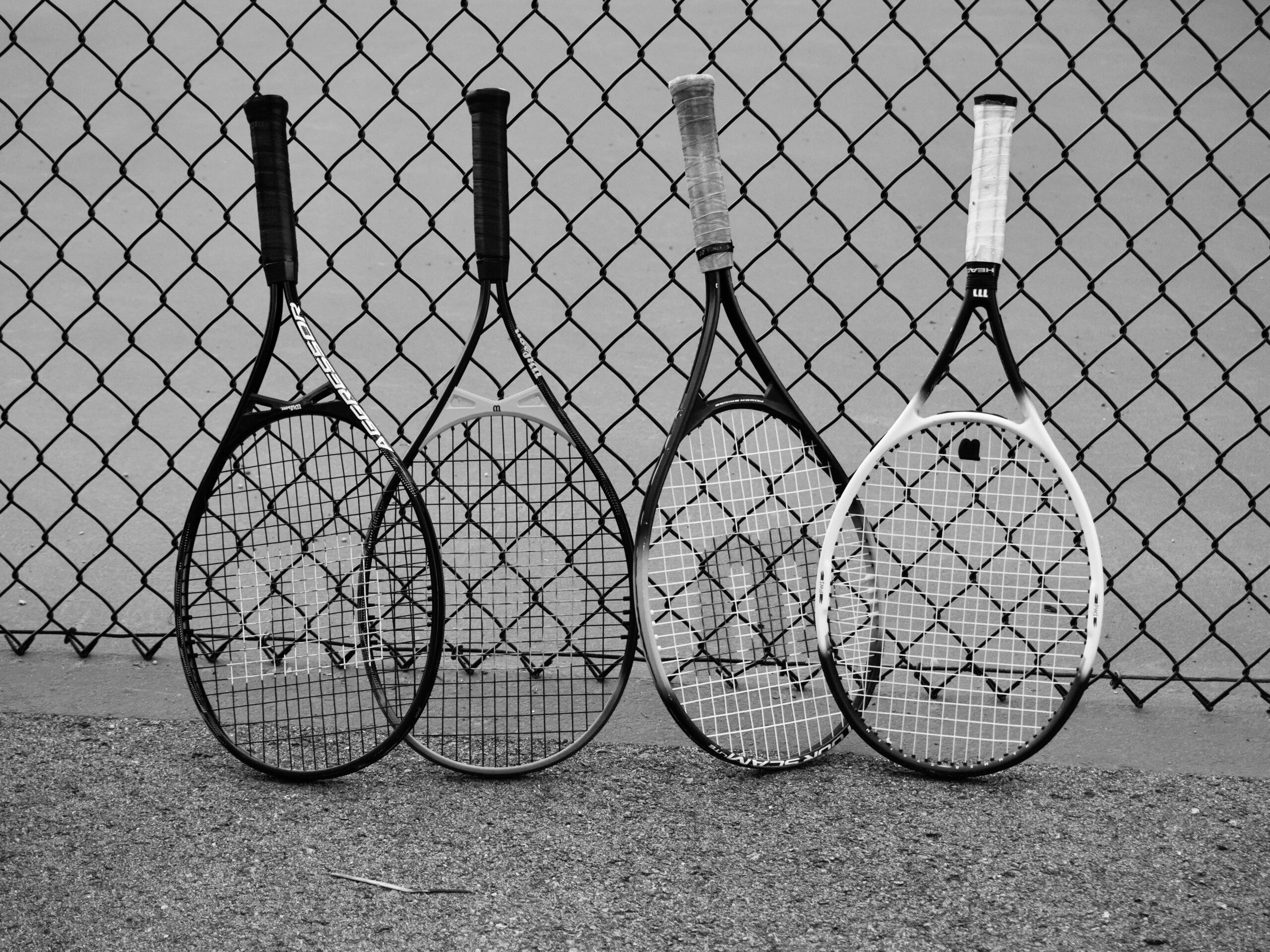 Vier tennisrackets leunen naast elkaar tegen een metalen hek.