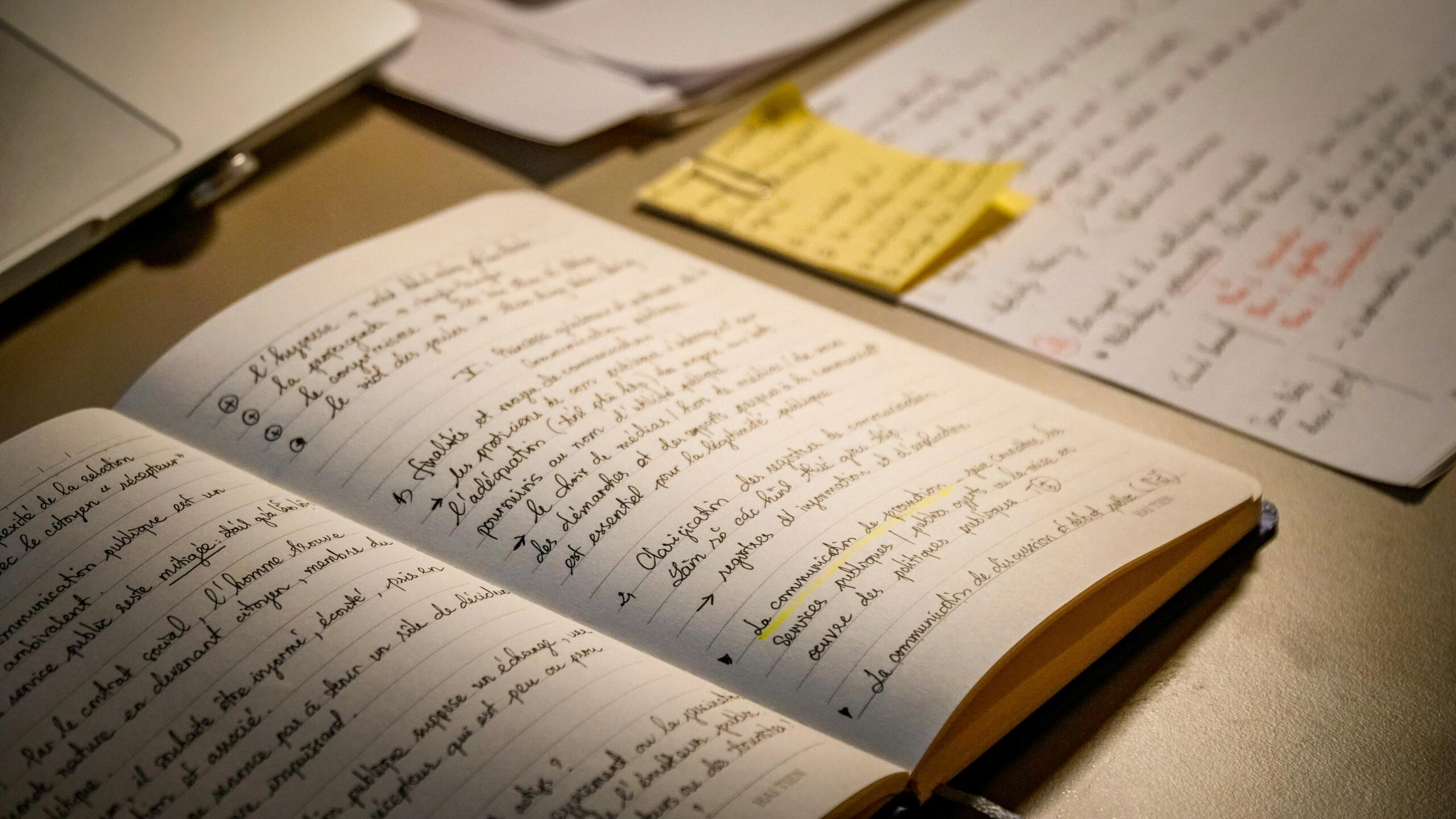 Een opengeslagen notitieboek met handgeschreven tekst ligt op een bureau.