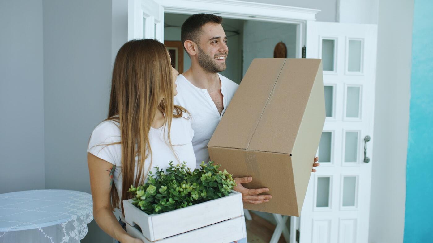 Een stel staat met verhuisdozen in de deuropening van een nieuwe woning.