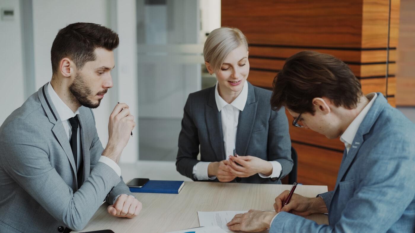 Drie zakelijke gesprekspartners bespreken een contract aan een vergadertafel.