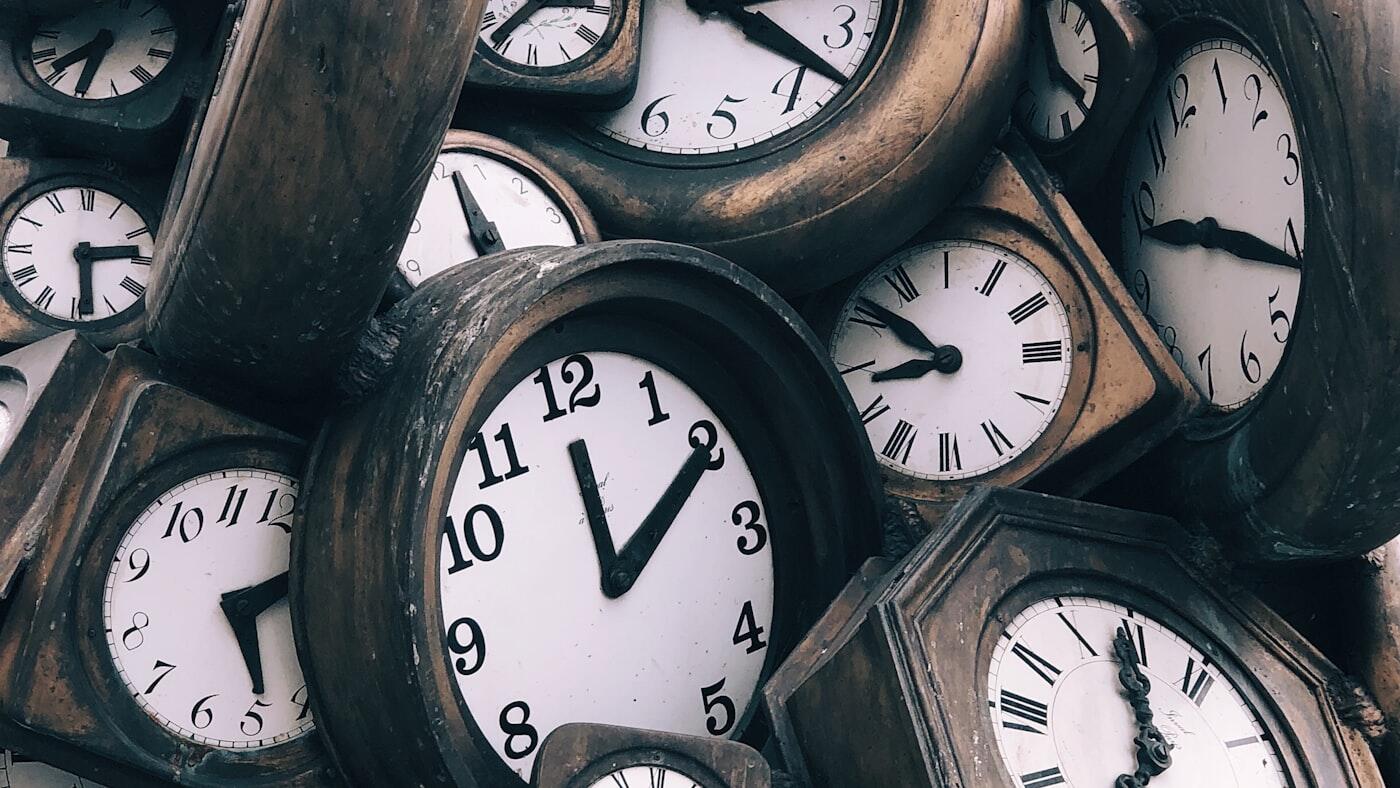 Meerdere analoge klokken hangen bij elkaar tegen een houten wand.