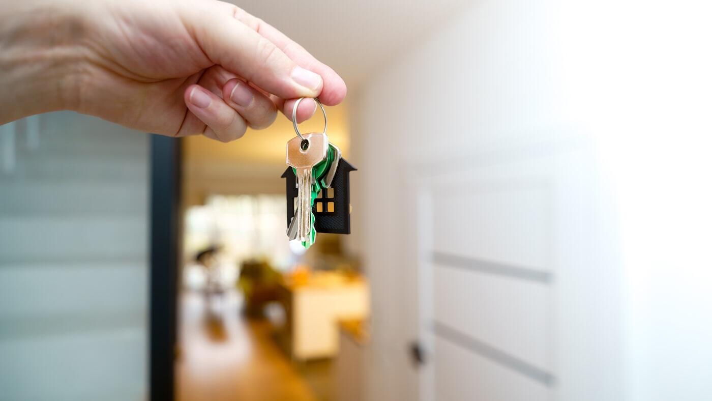 Een hand houdt een huissleutel voor een lichte woonruimte.