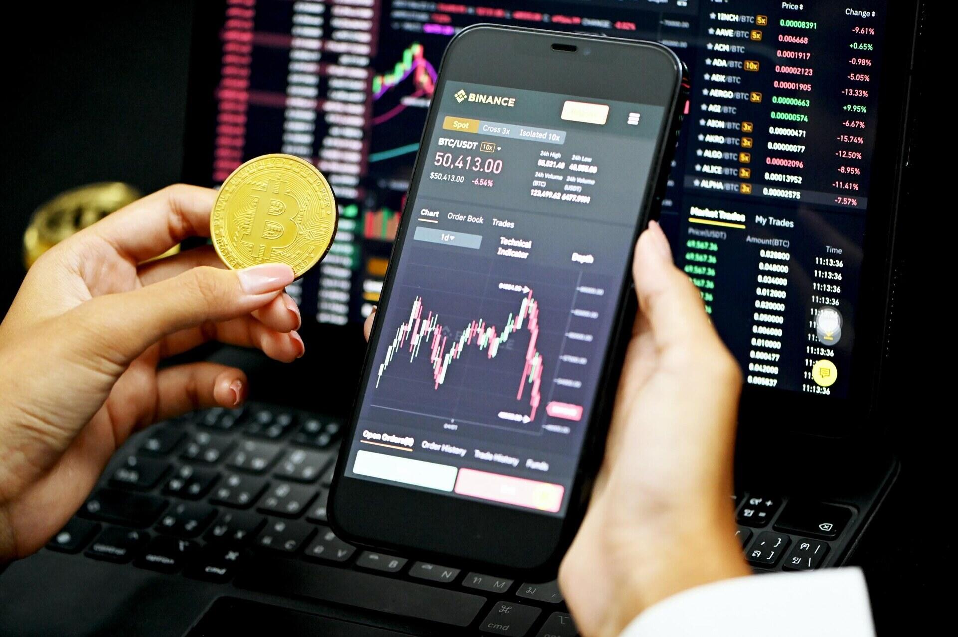 Persoon houdt een munt en smartphone voor schermen met cryptokoersen