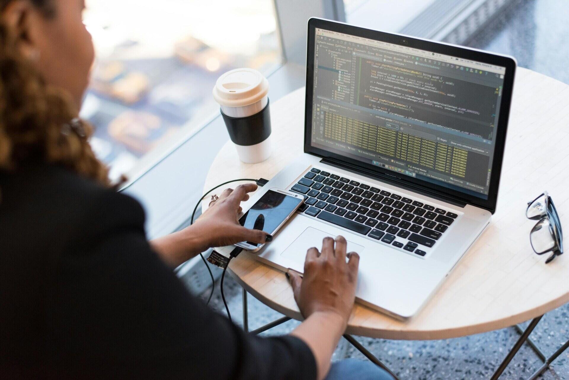 Persoon gebruikt een laptop en houdt een smartphone vast.