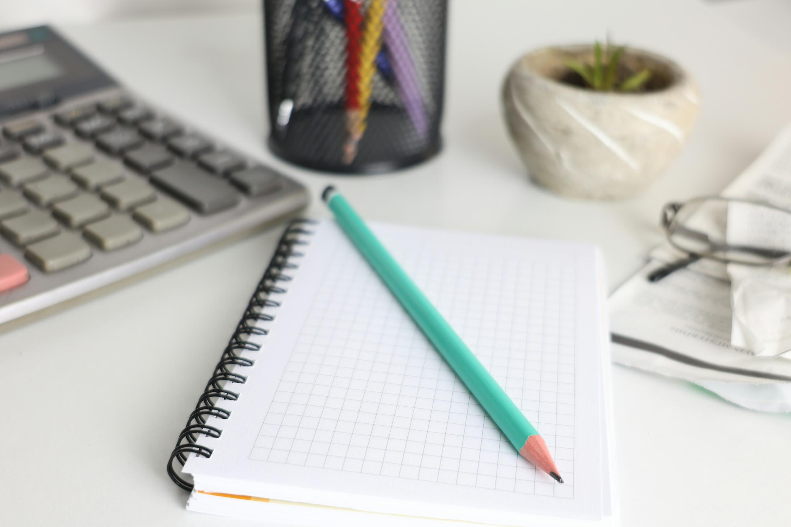Calculator naast een notitieboek en potlood op een bureau