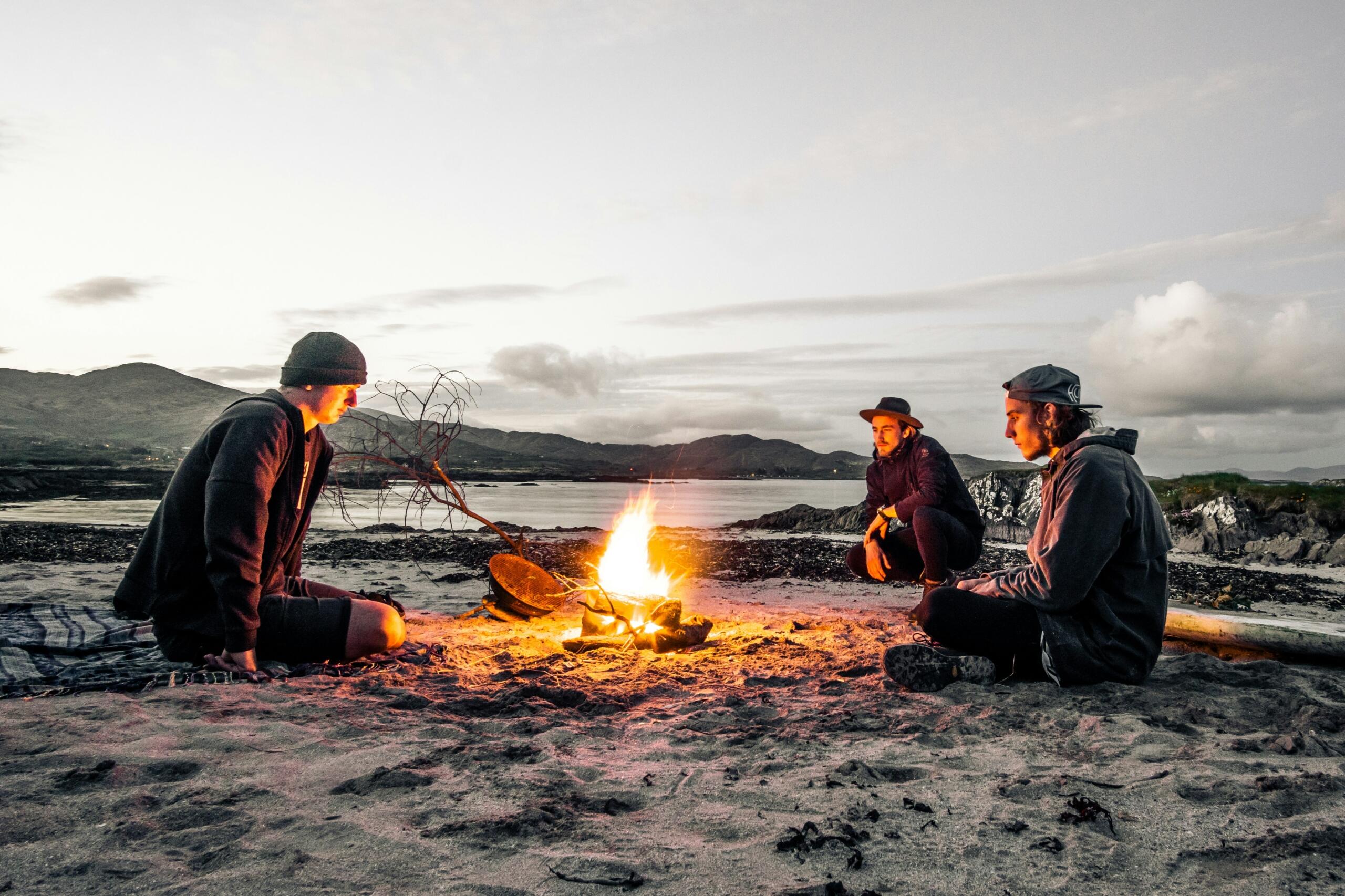 Drie mensen rond een vuur aan de kust in Ierland