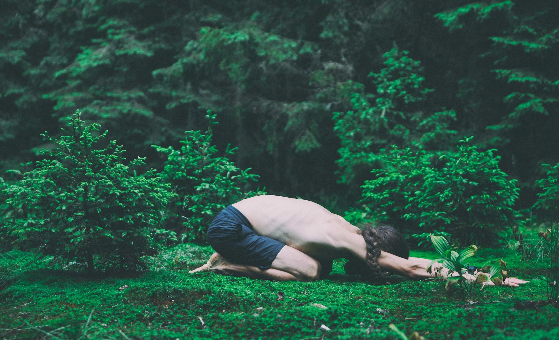 Mann ligger på gress i skogen i barnets posisjon yoga