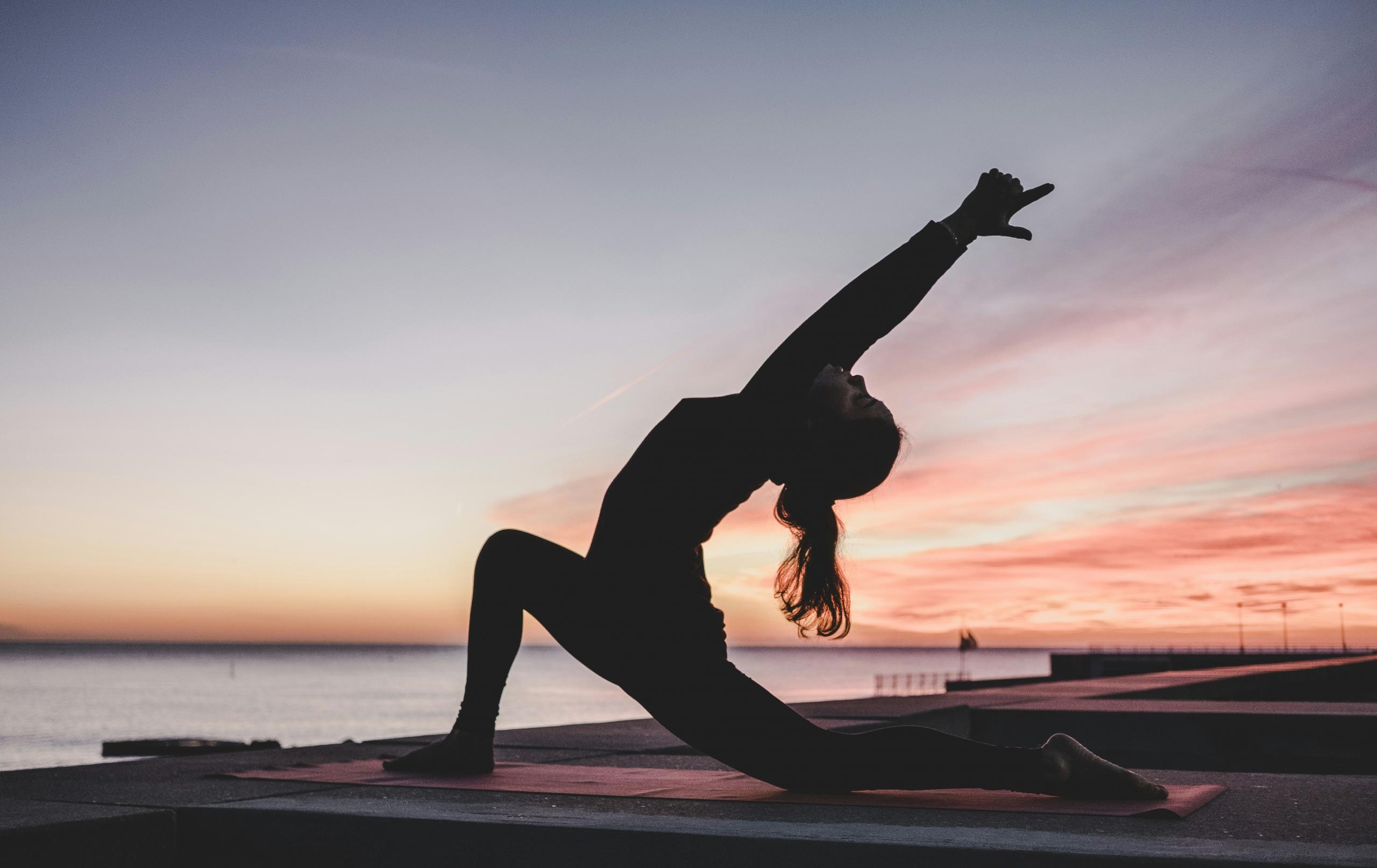 En person som gjør yoga med solnedgang i bakgrunnen.