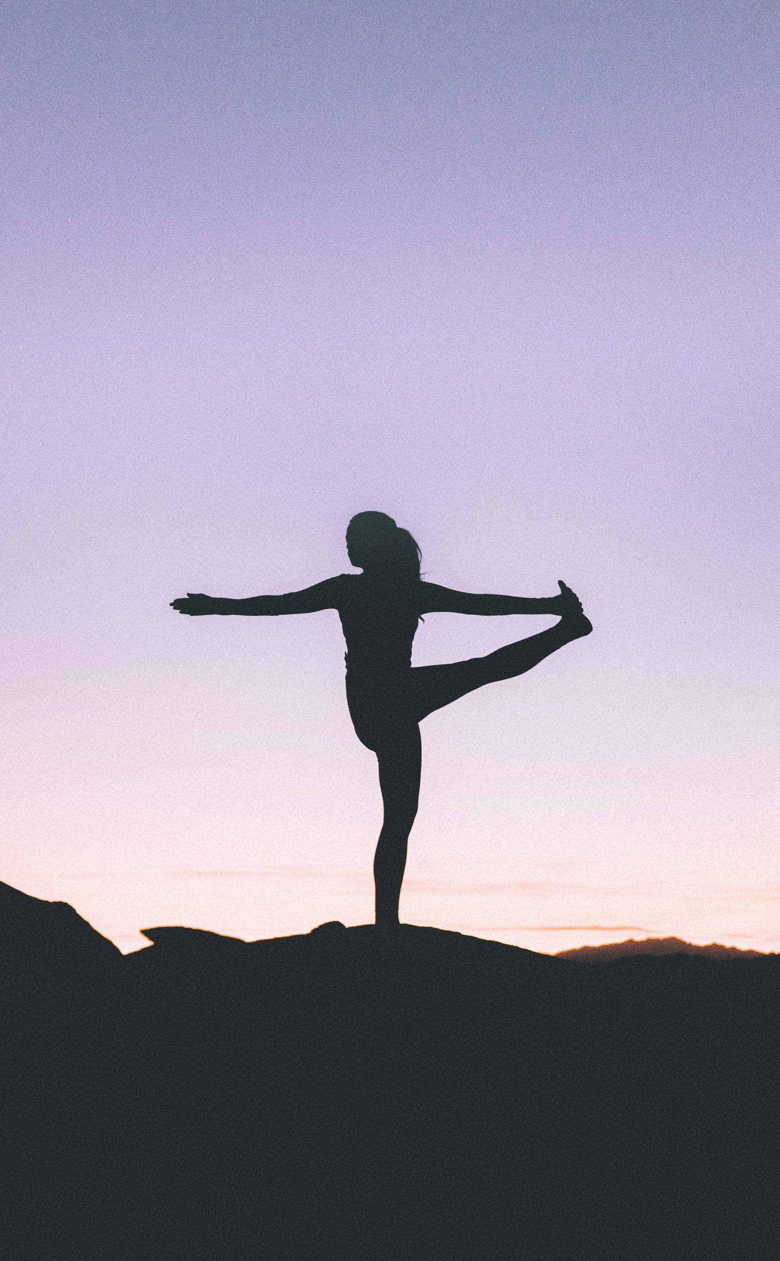 Kvinne står på ett ben i yoga-stilling foran en utsikt