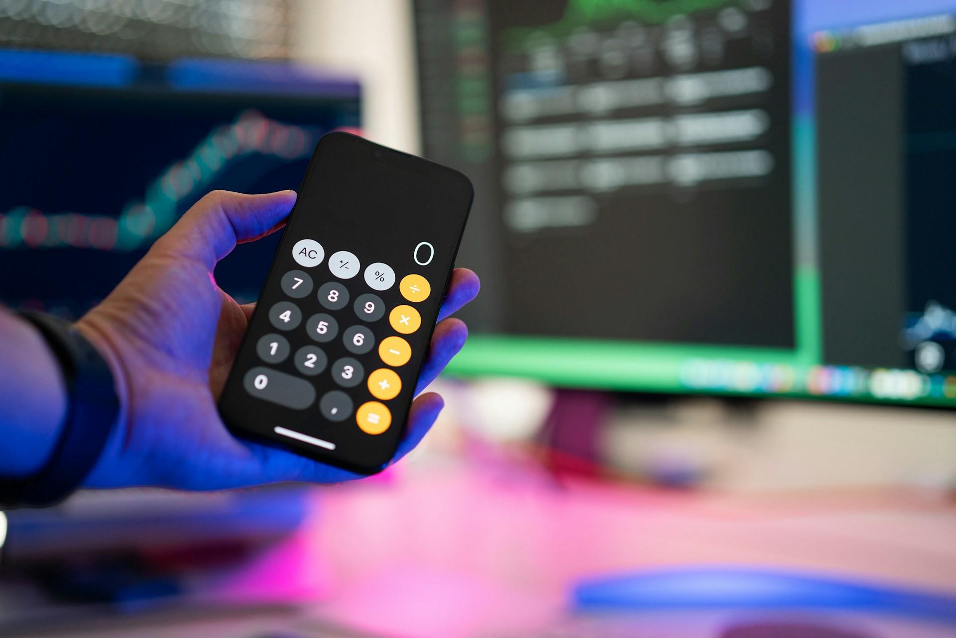 Kalkulator fra telefon holdes i hånd foran PC-skjerm