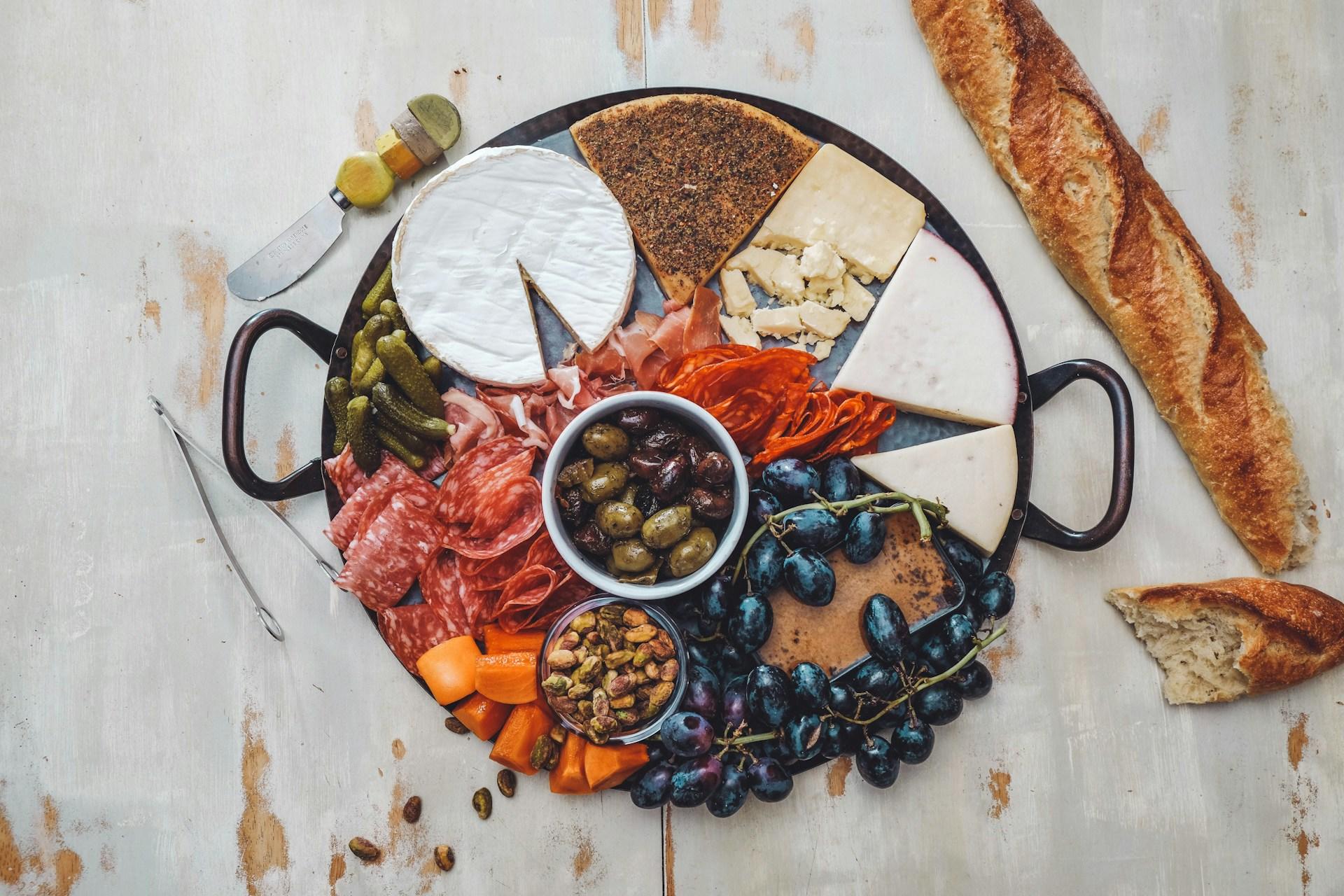 Ostefat med ulike typer oster, druer, oliven, kjøttpålegg og annet tilbehør.