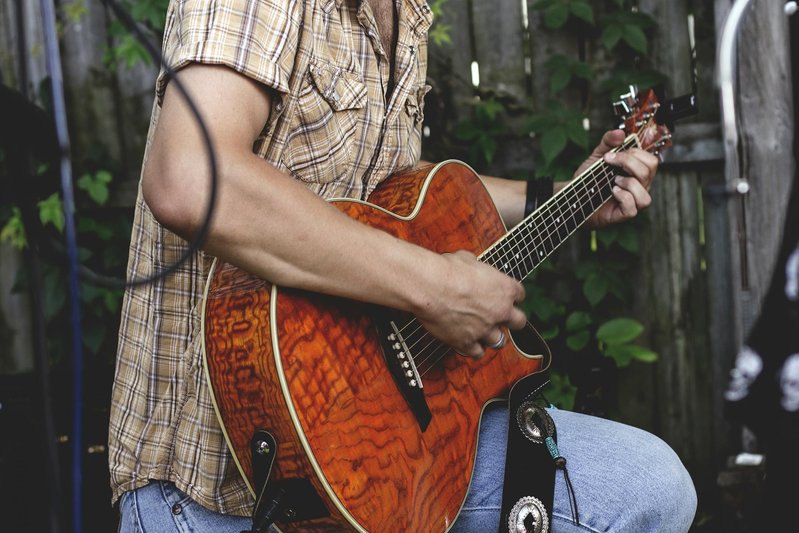 Person som spiller på en brun gitar.