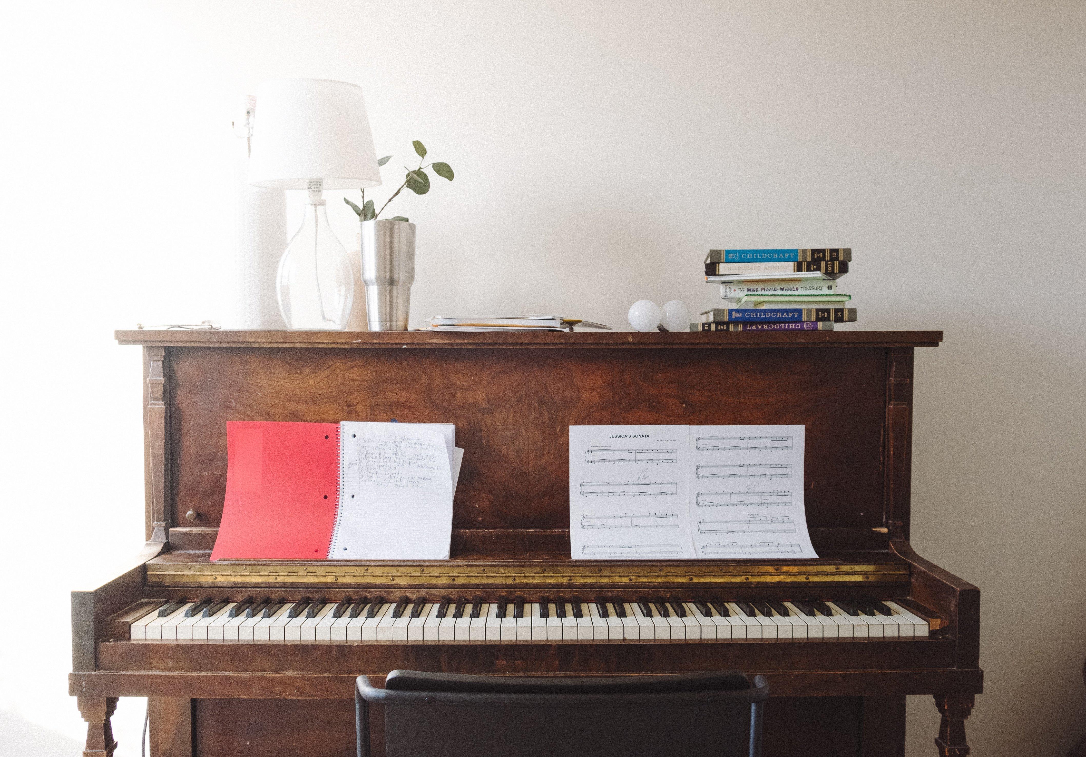 Et piano står inntil en hvit vegg, oppå det står bøker, en plante og en lampe