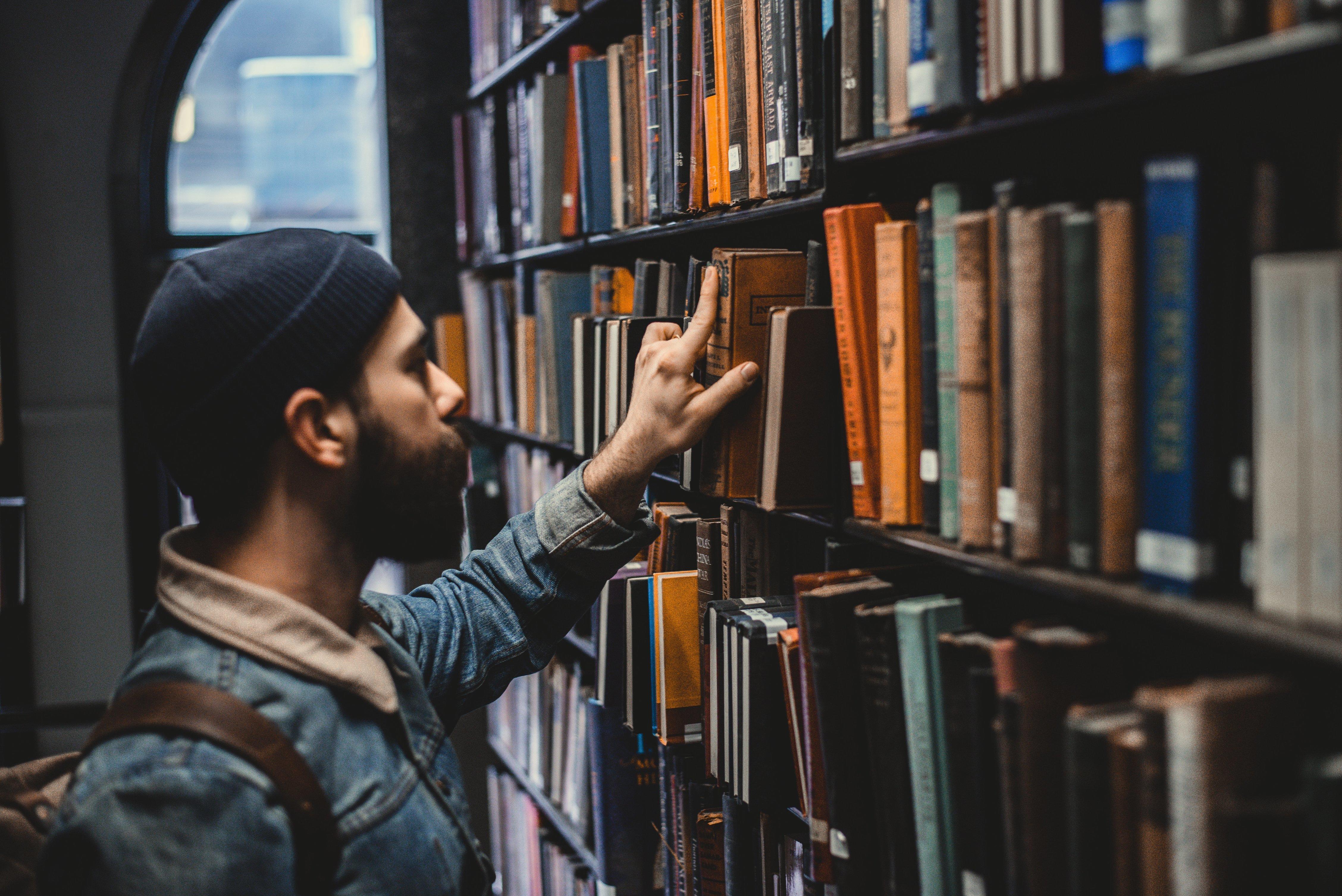 En mann plukker ut en bok fra en hylle i et bibliotek