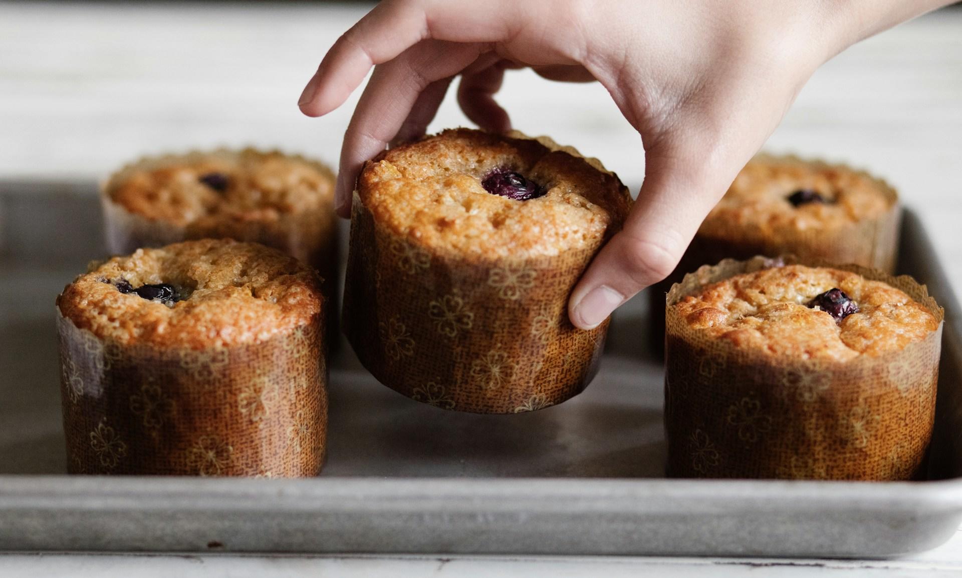 Hånd løfter opp en muffins med rødt fyll fra bakebrett.