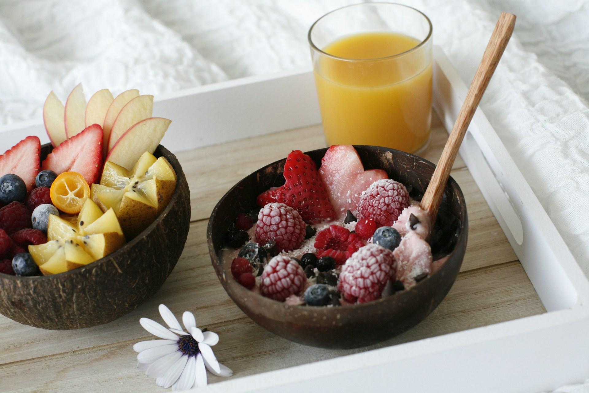 Fargerik frokost bestående av juice, og skåler med frukt og yoghurt på et fat.
