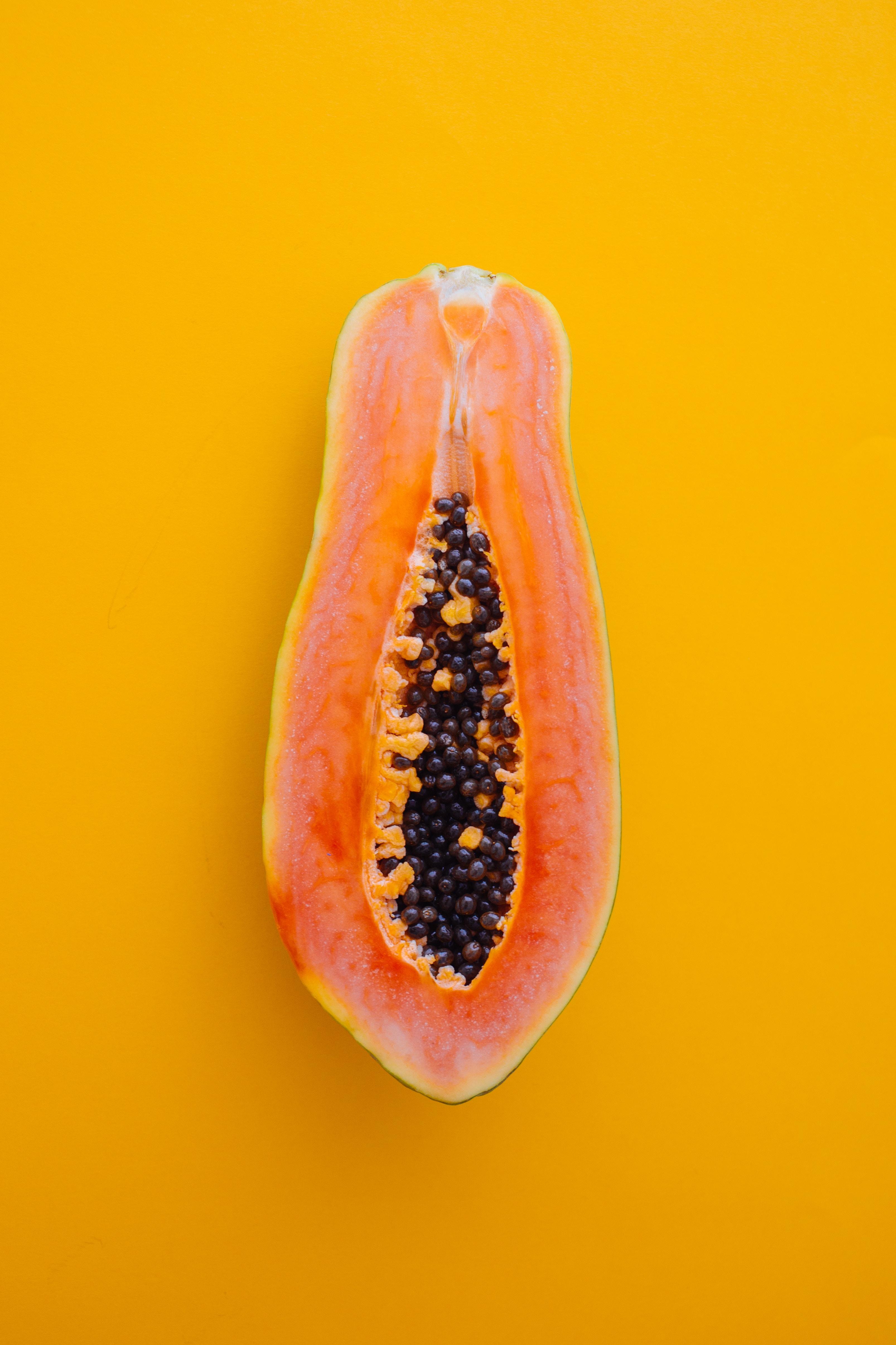 en halv papaya rett ovenfra, på en gul bakgrunn