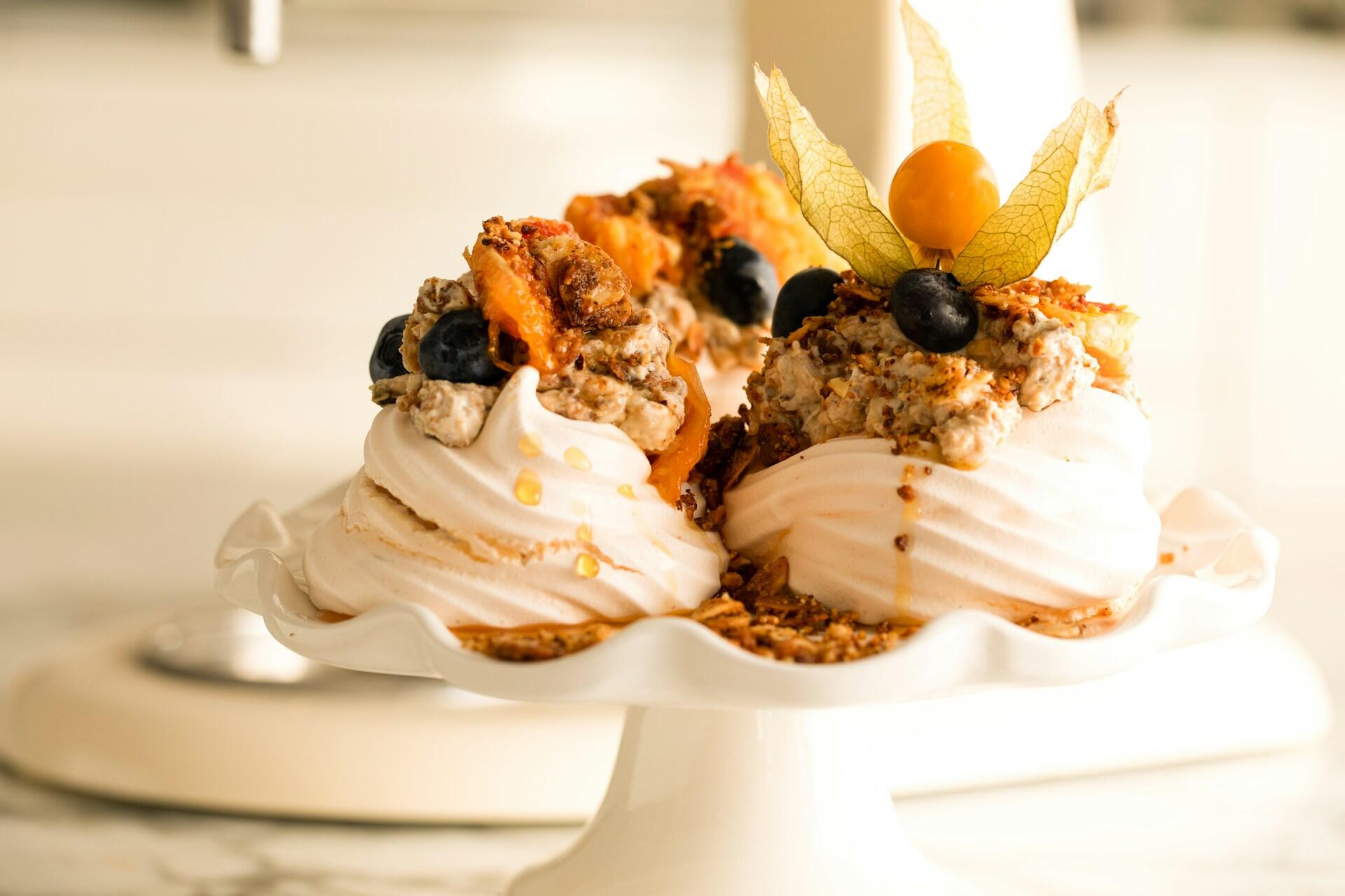 Pavlova med frukt og pynt dandert på høyt hvitt fat.