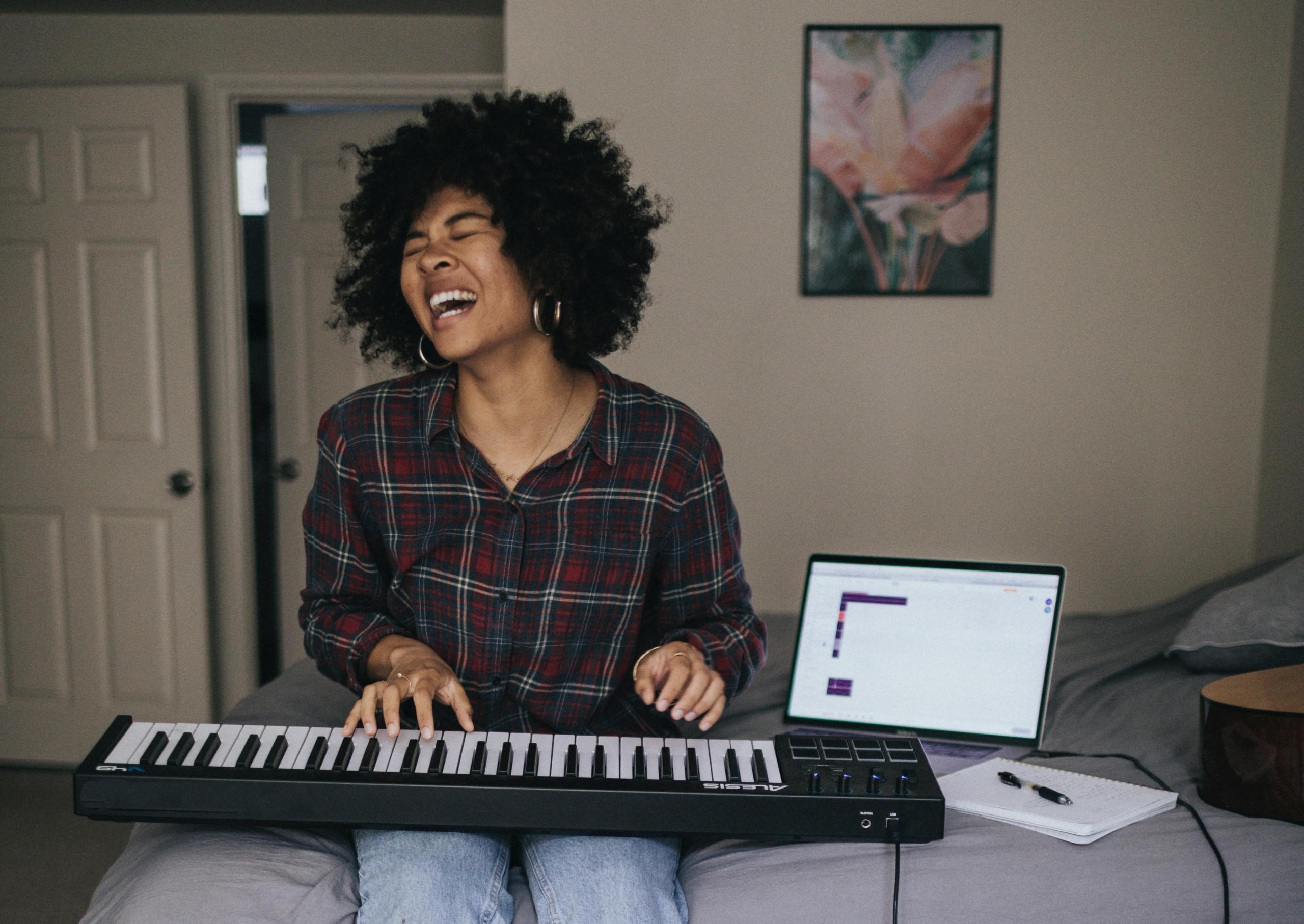 Kvinne sitter på soverommet med et keyboard på fanget og synger høyt