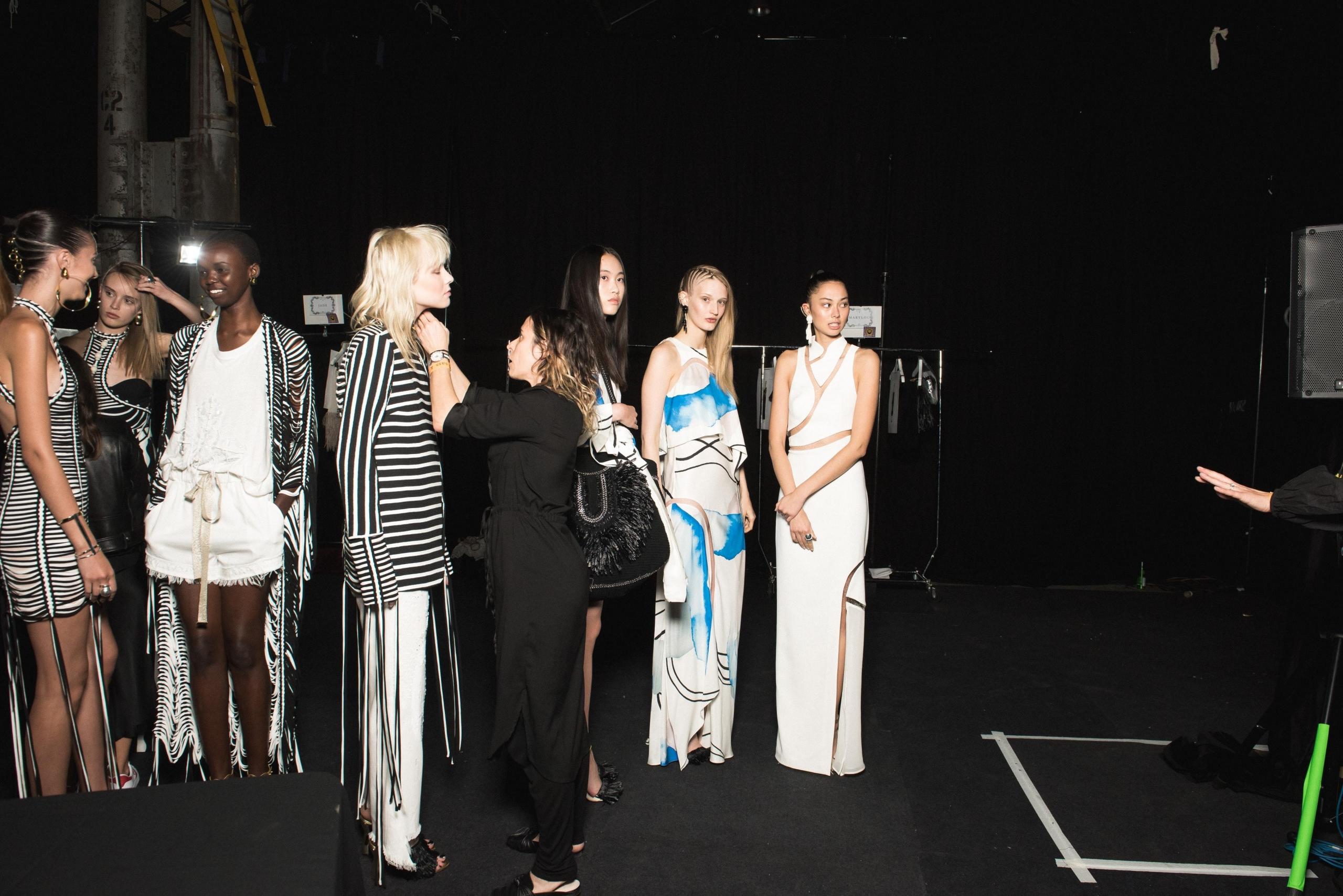 en designer er backstage sammen med modellene og retter på et antrekk