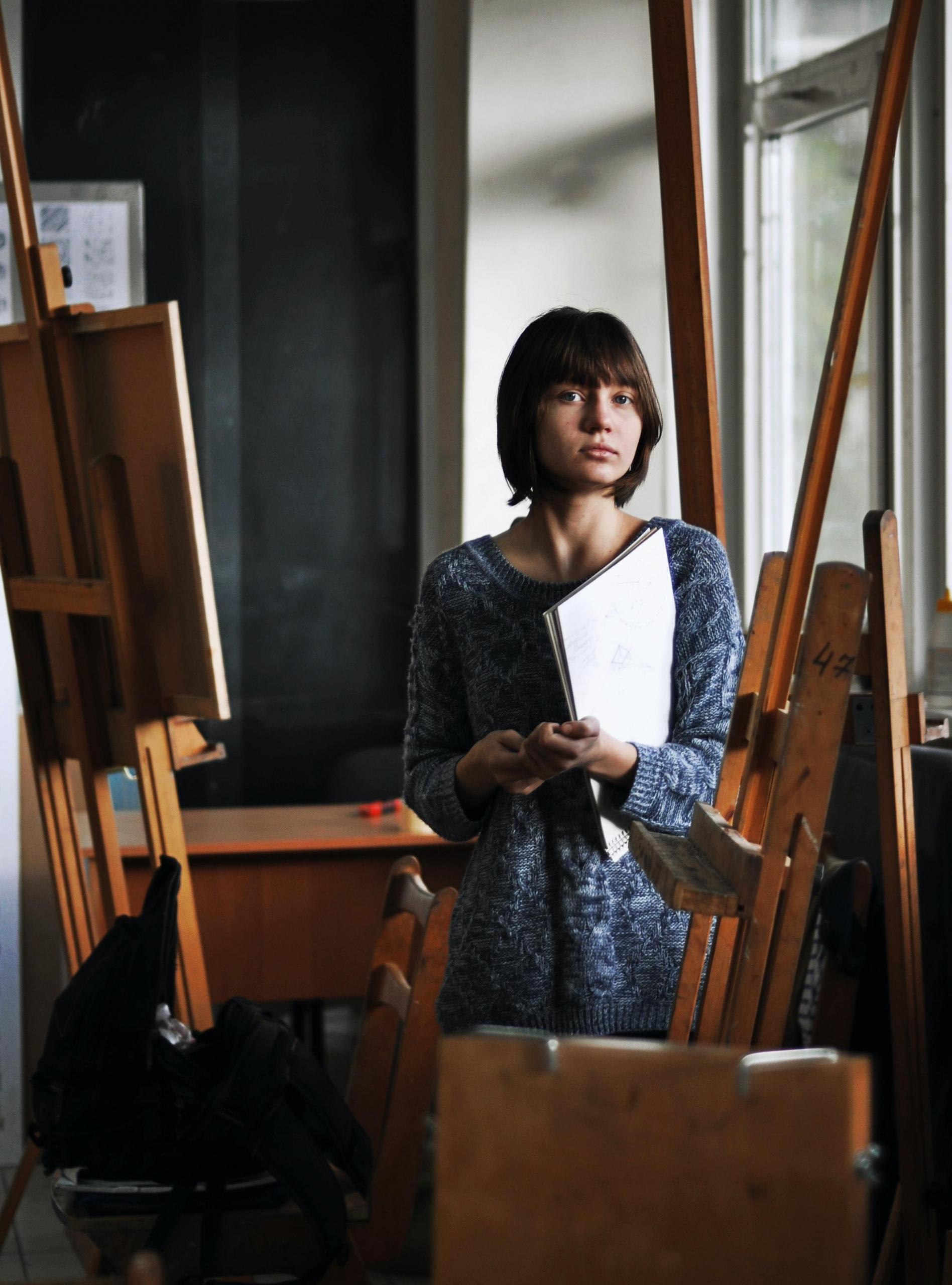 en jente står i et kunststudio og holder en blokk, rundt henne står staffelier