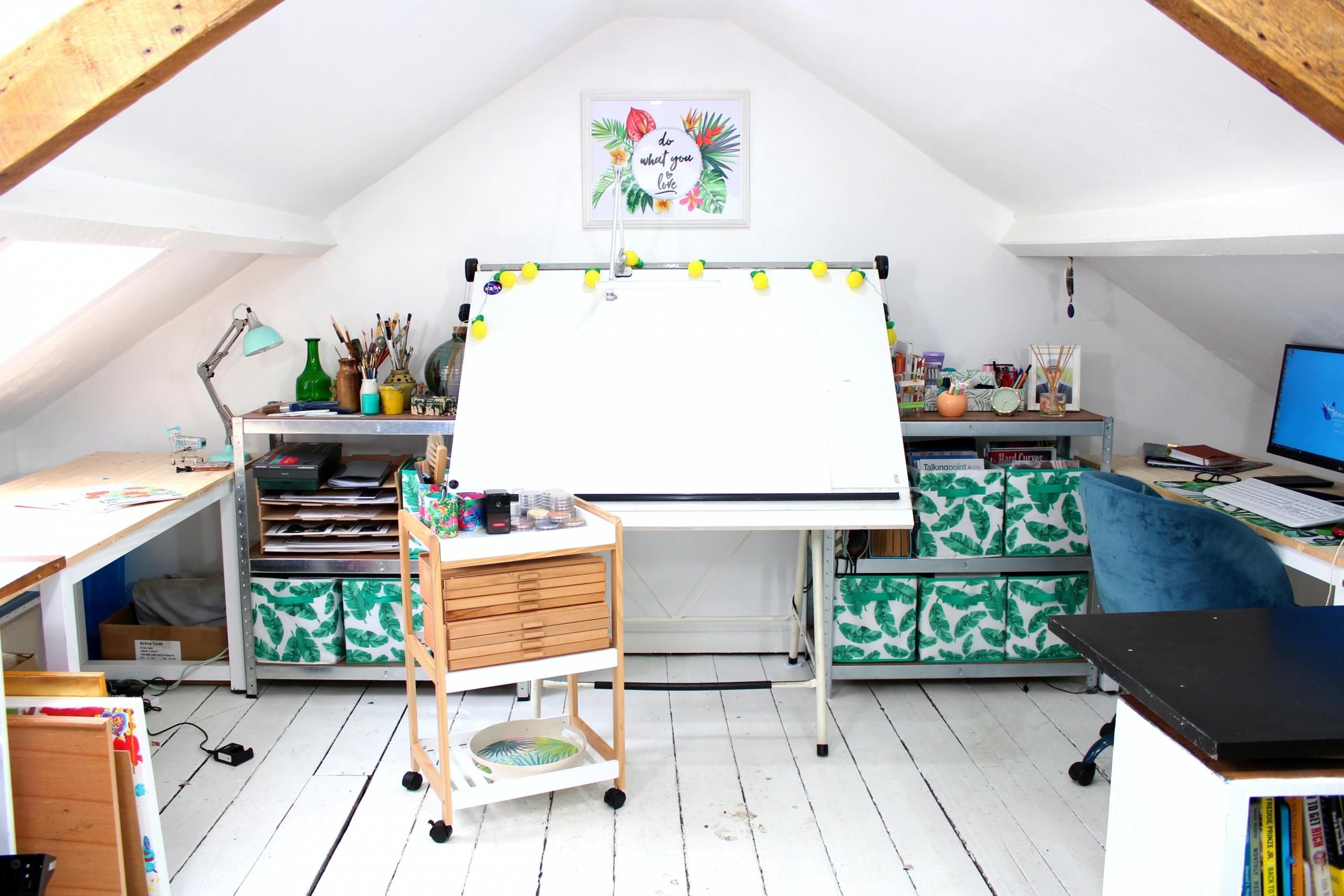 et kunststudio med skråtak og hvite vegger, pulter ved veggene og et tegnebord midt i bildet