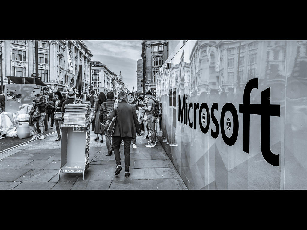 svart-hvitt-bilde av et folksomt fortau og et stort microsoft-skilt