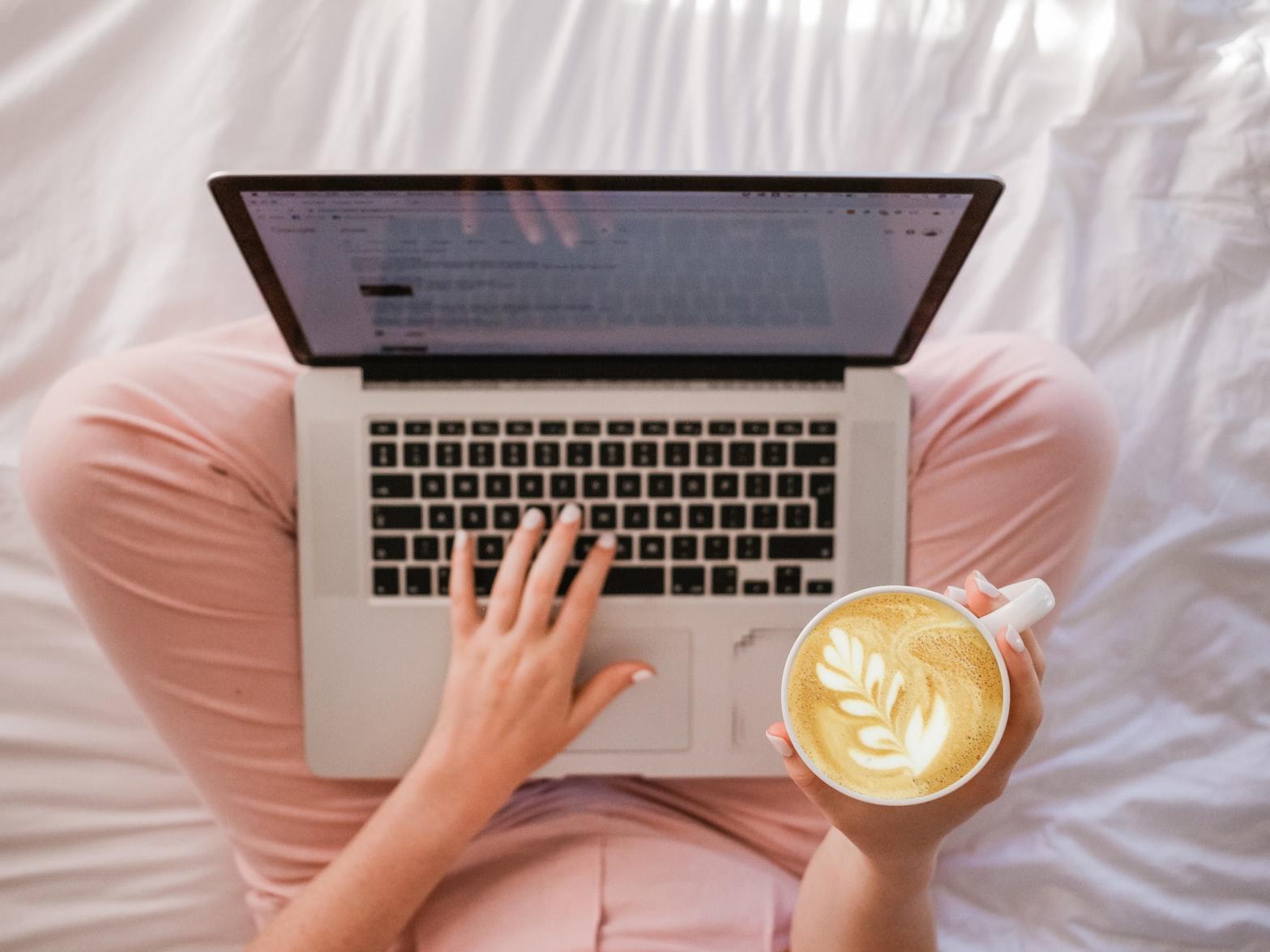 En person sitter med laptop på fanget og en kaffekopp i hånda.
