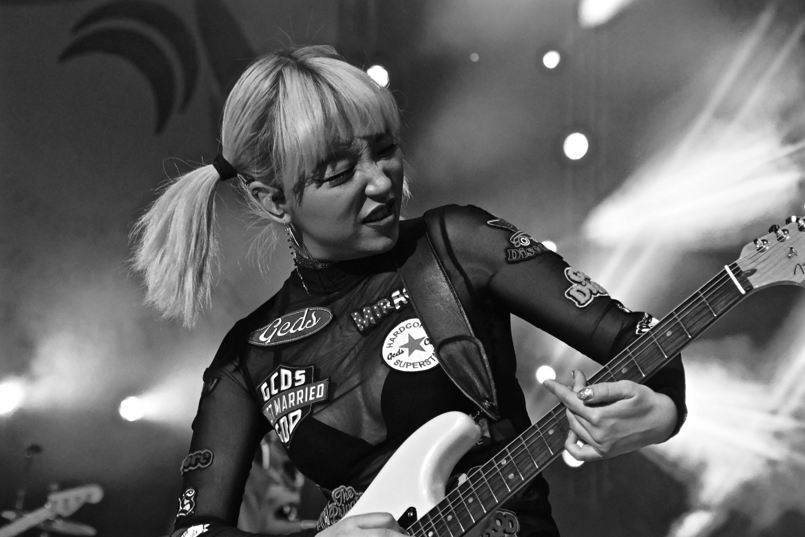 En ung kvinne spiller gitar på en scene, hun ser ut som hun både konsentrerer og koser seg
