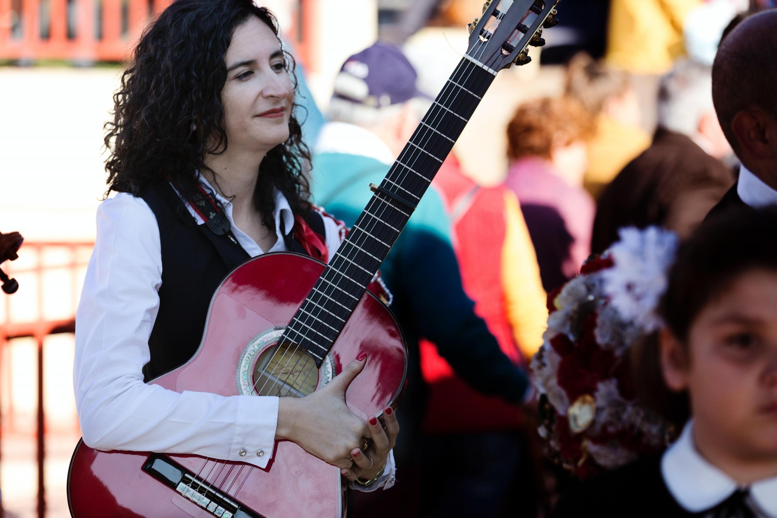 en kvinne står ute på et folksomt sted, hun holder en rød gitar