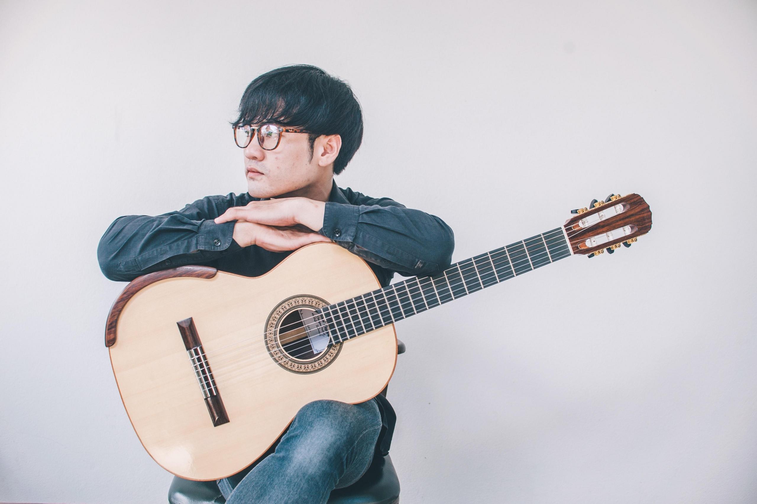 ung mann sitter med en gitar på fanget, lener armene på gitaren og ser tankefullt ut i lufta
