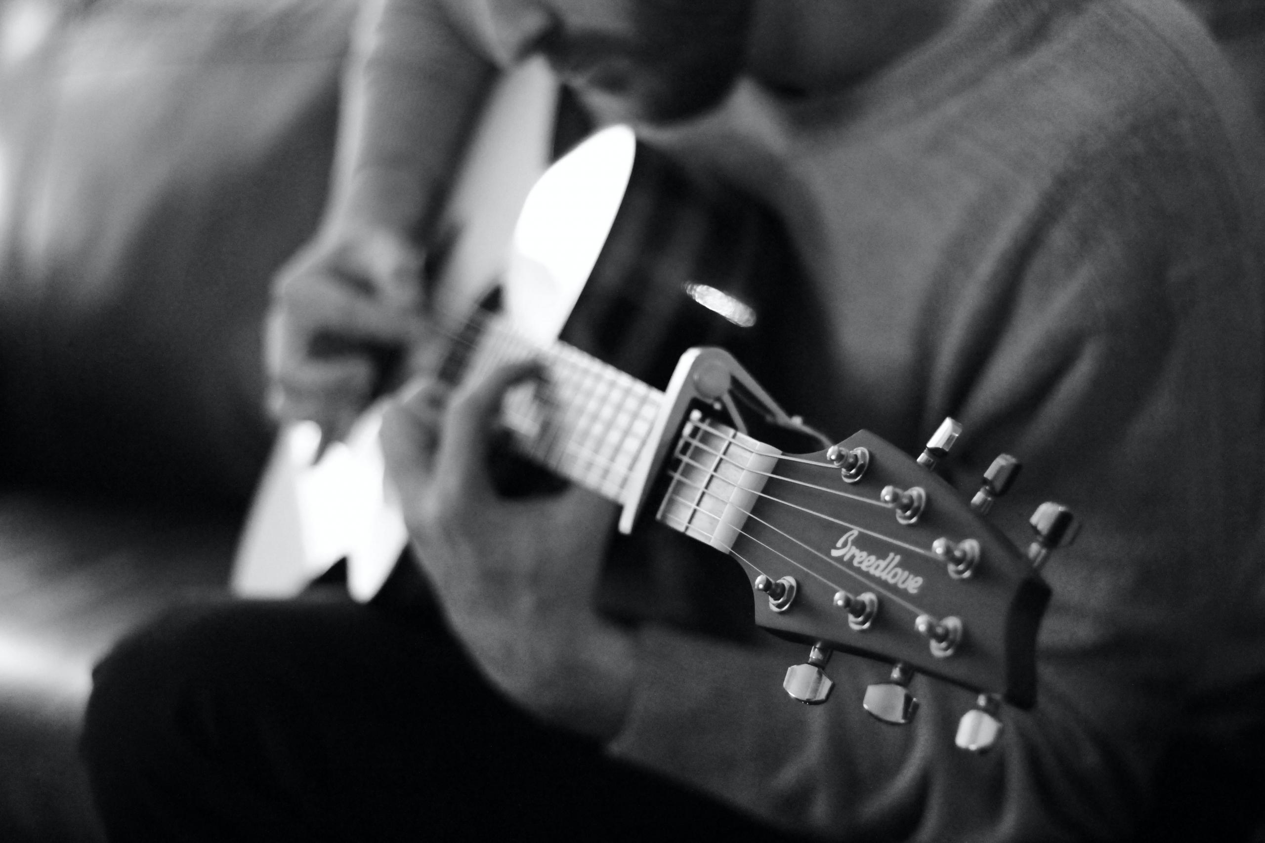 en mann spiller gitar, svart-hvitt-foto med smalt fokus tatt fra siden