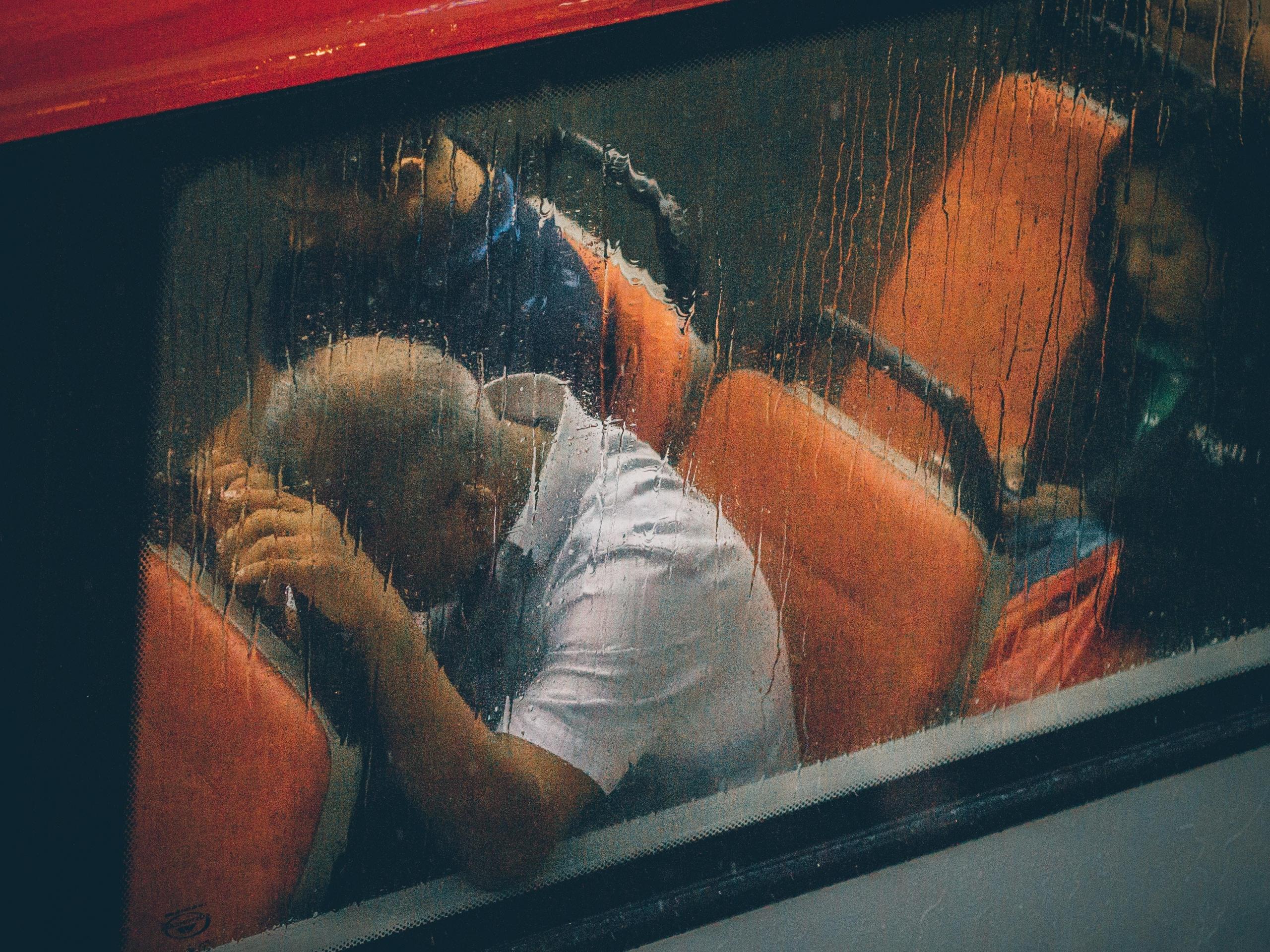 bilde gjennom en regndekket bussrute av en mann som lener pannen mot setet foran