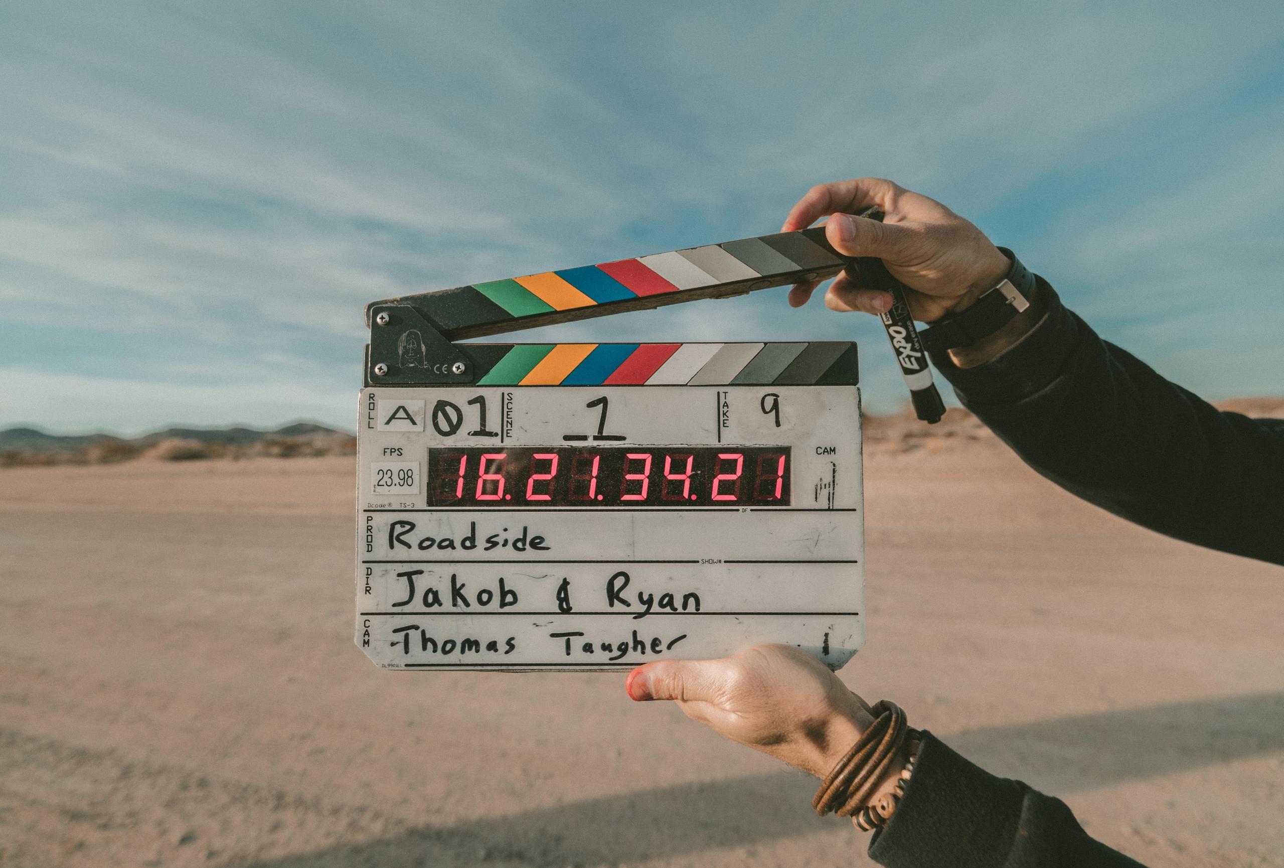 En filmklapper med informasjon om en scene holdes opp foran kamera, foran et tørt, flatt landskap