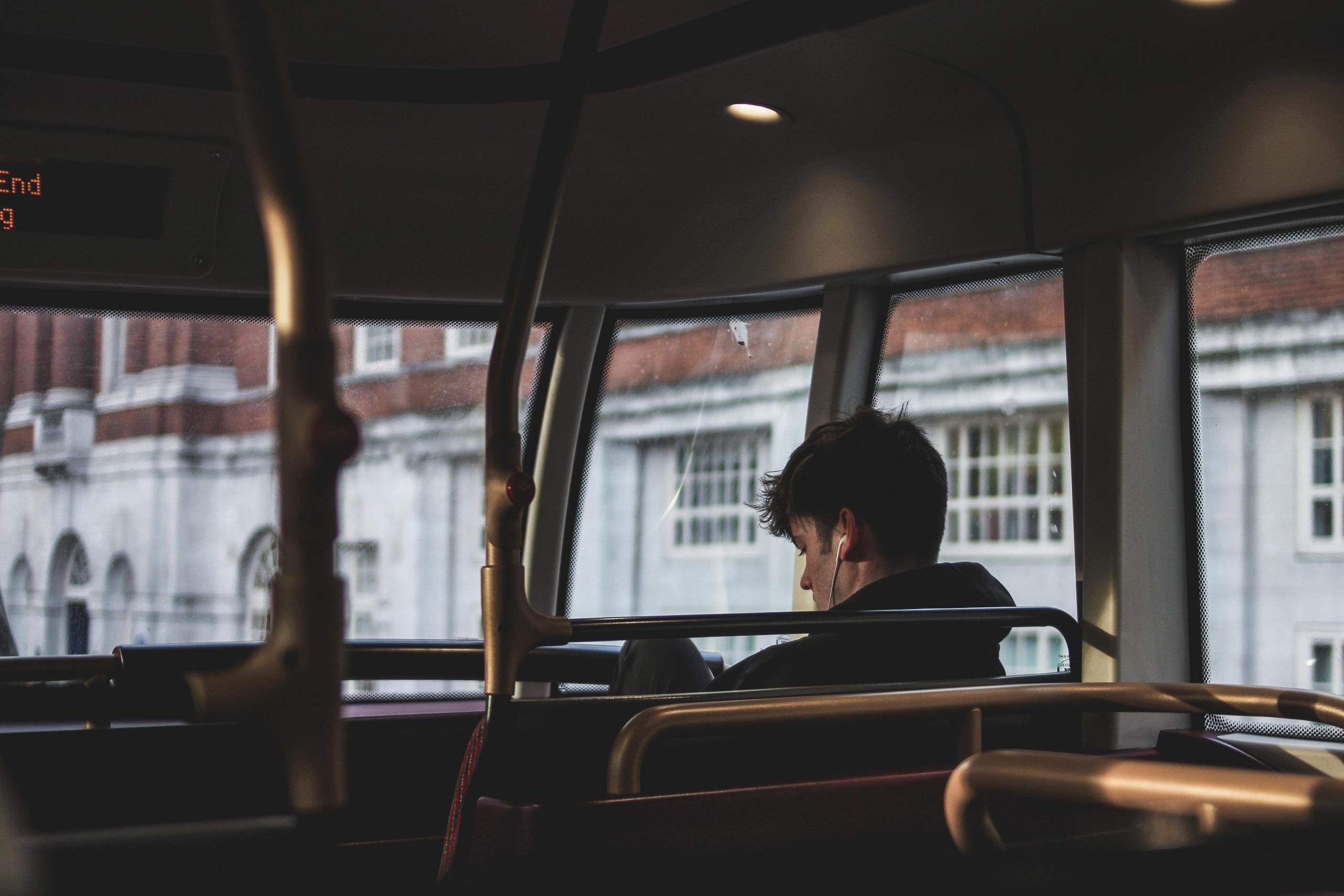 en ung mann sitter på en buss og hører på noe med øretelefoner