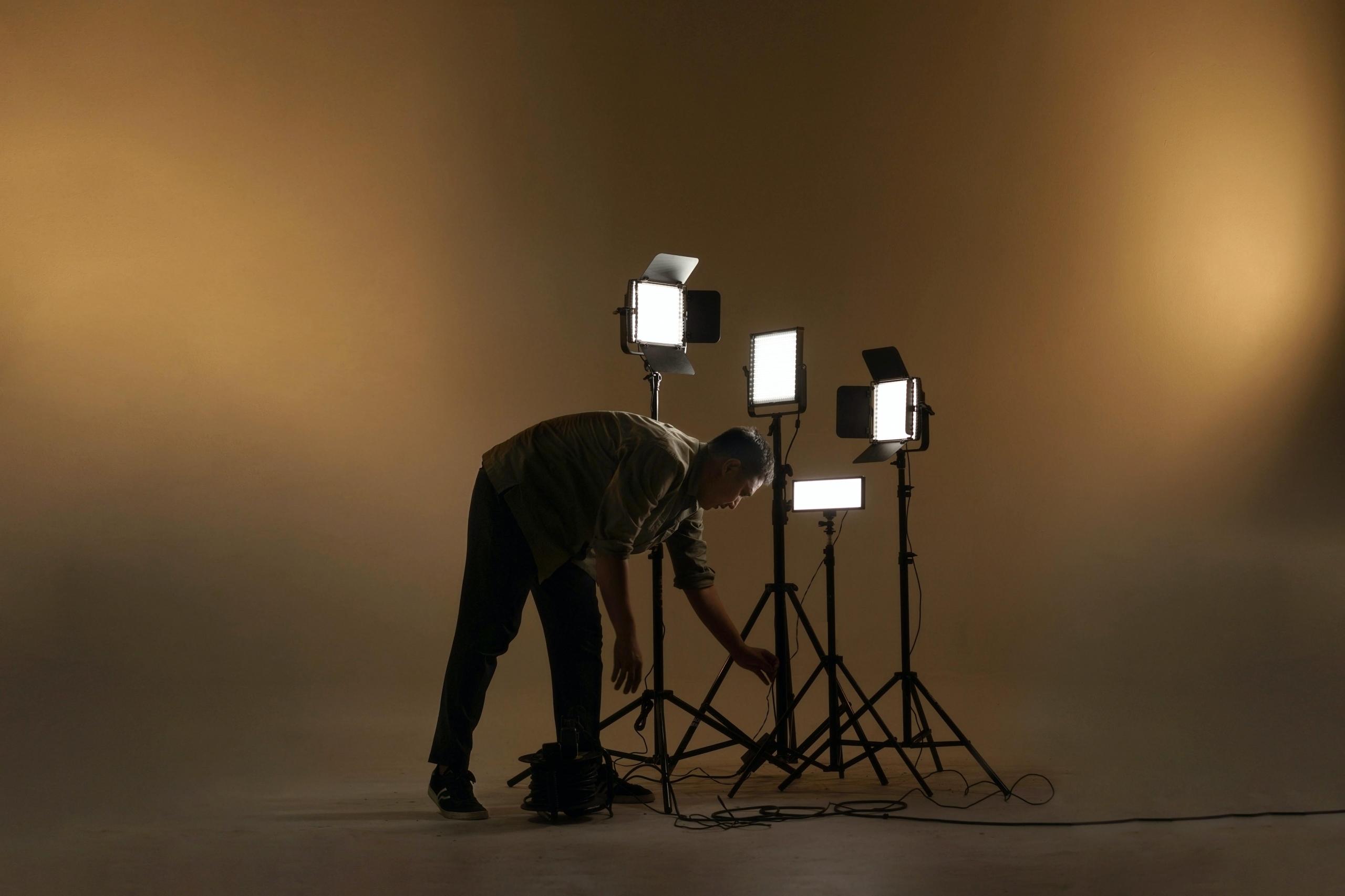 en mann står i et dunkelt belyst foto- eller filmstudio og ordner med en samling av lyskastere