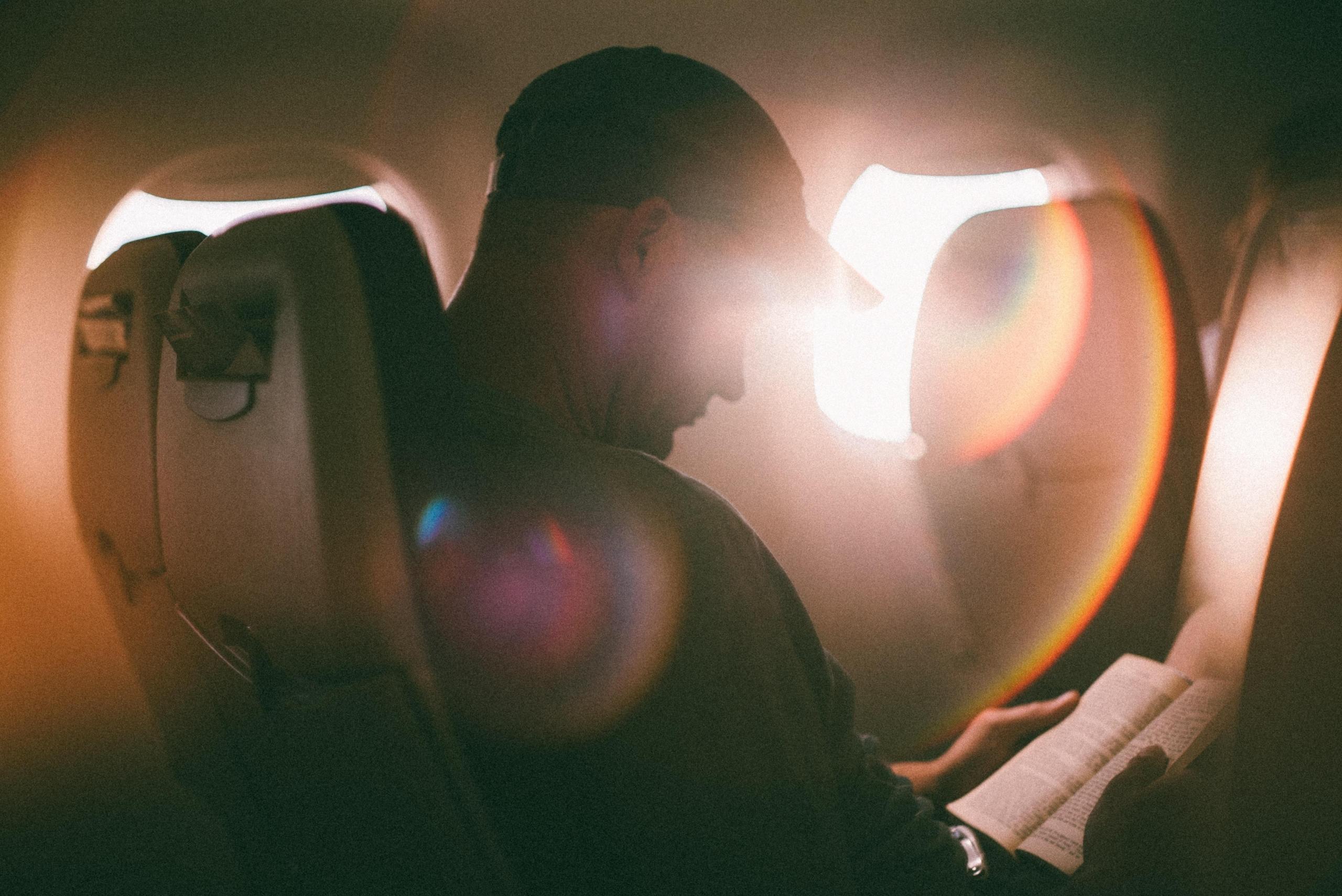 en mann sitter på et fly og leser, sola skinner inn gjennom vinduet
