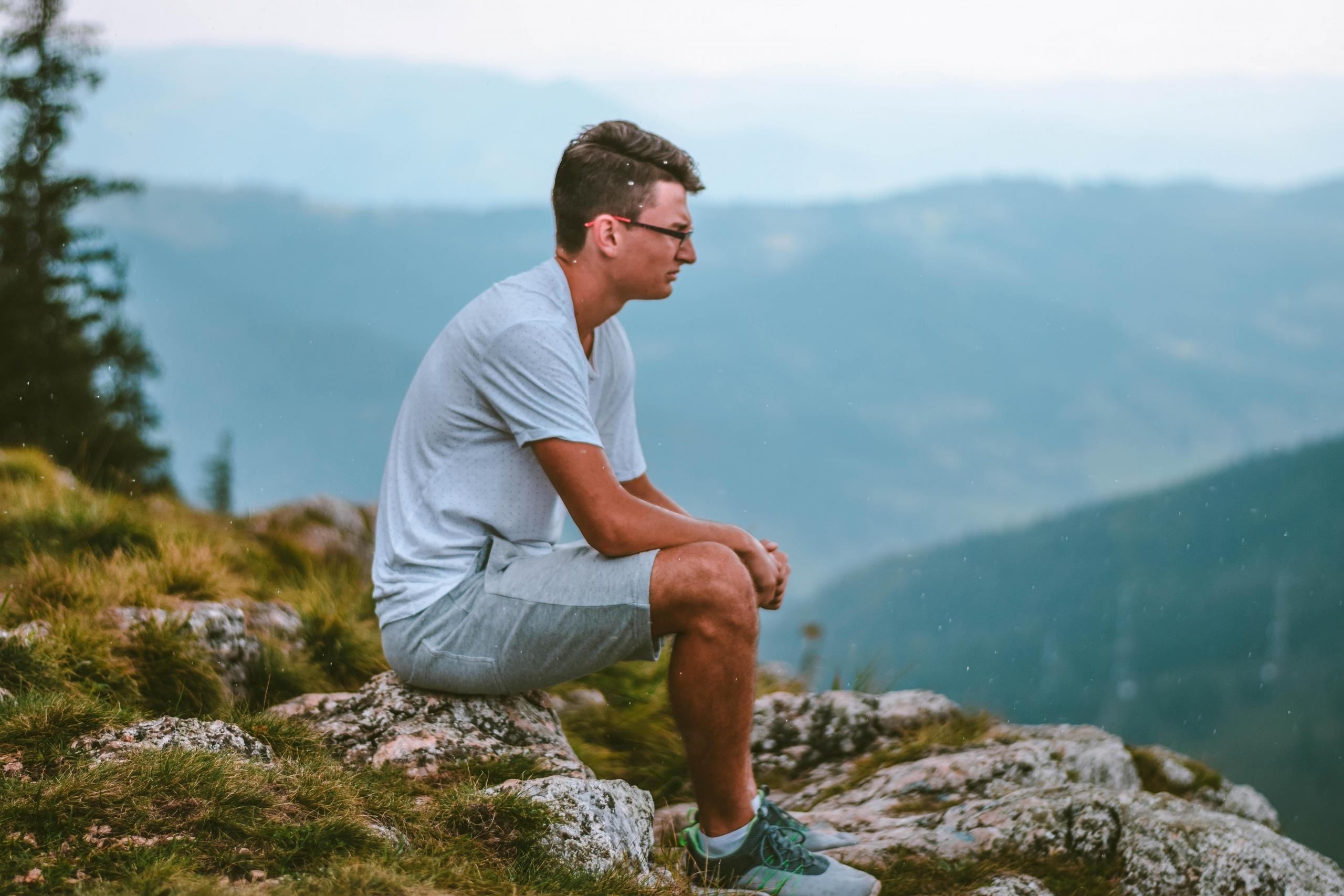 en ung mann sitter på en stein på et fjell, i bakgrunnen ligger bleke åser bak hverandre