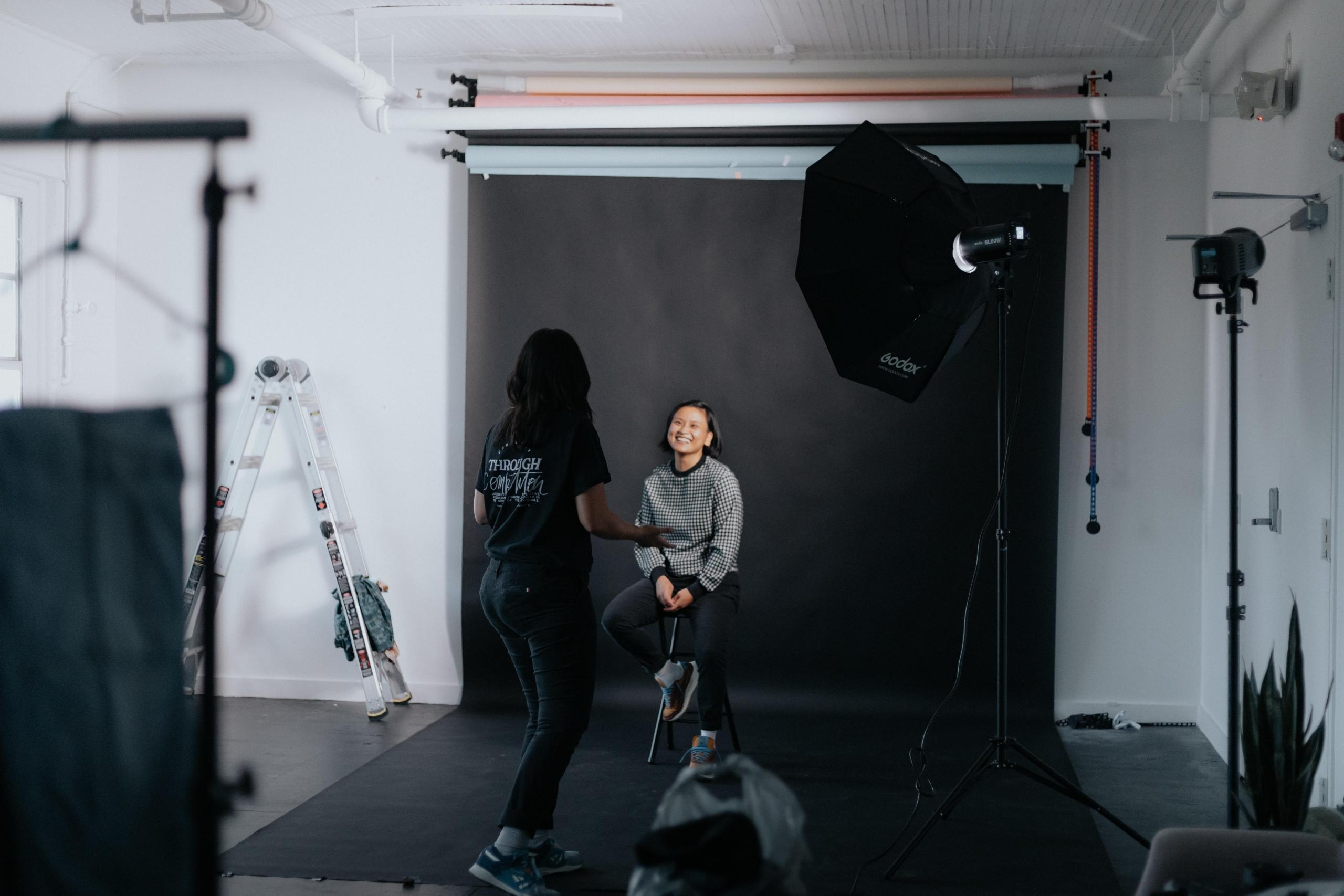 En kvinne fotograferer en annen i et fotostudio med svart bakgrunn