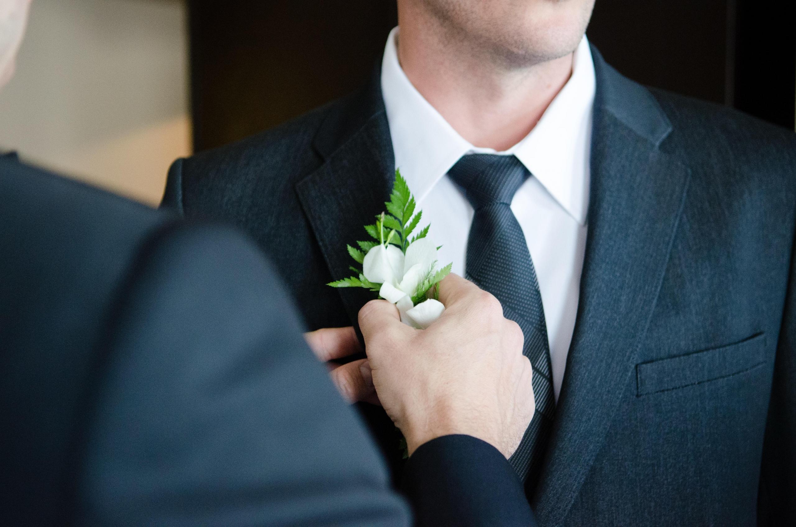 en person fester en hvit blomsterbrosje til dressen til en brudgom