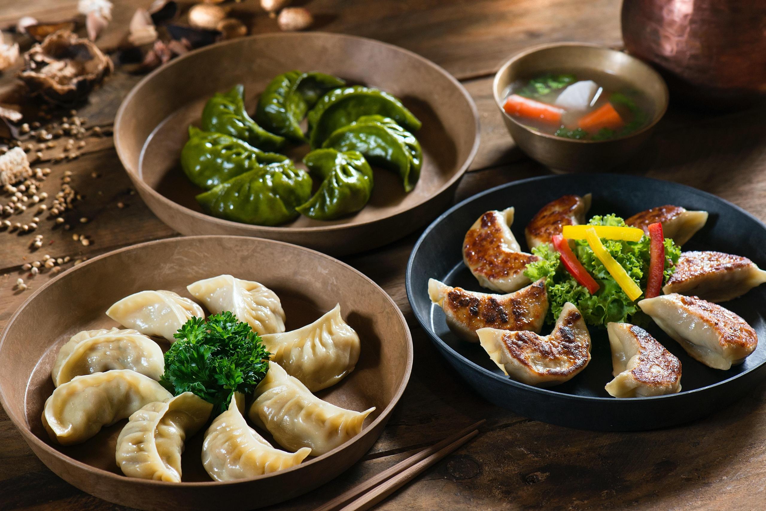 forskjellige typer dumplings, noen dampet, noen stekt, noen grønne, ligger i forskjellige skåler på et bord