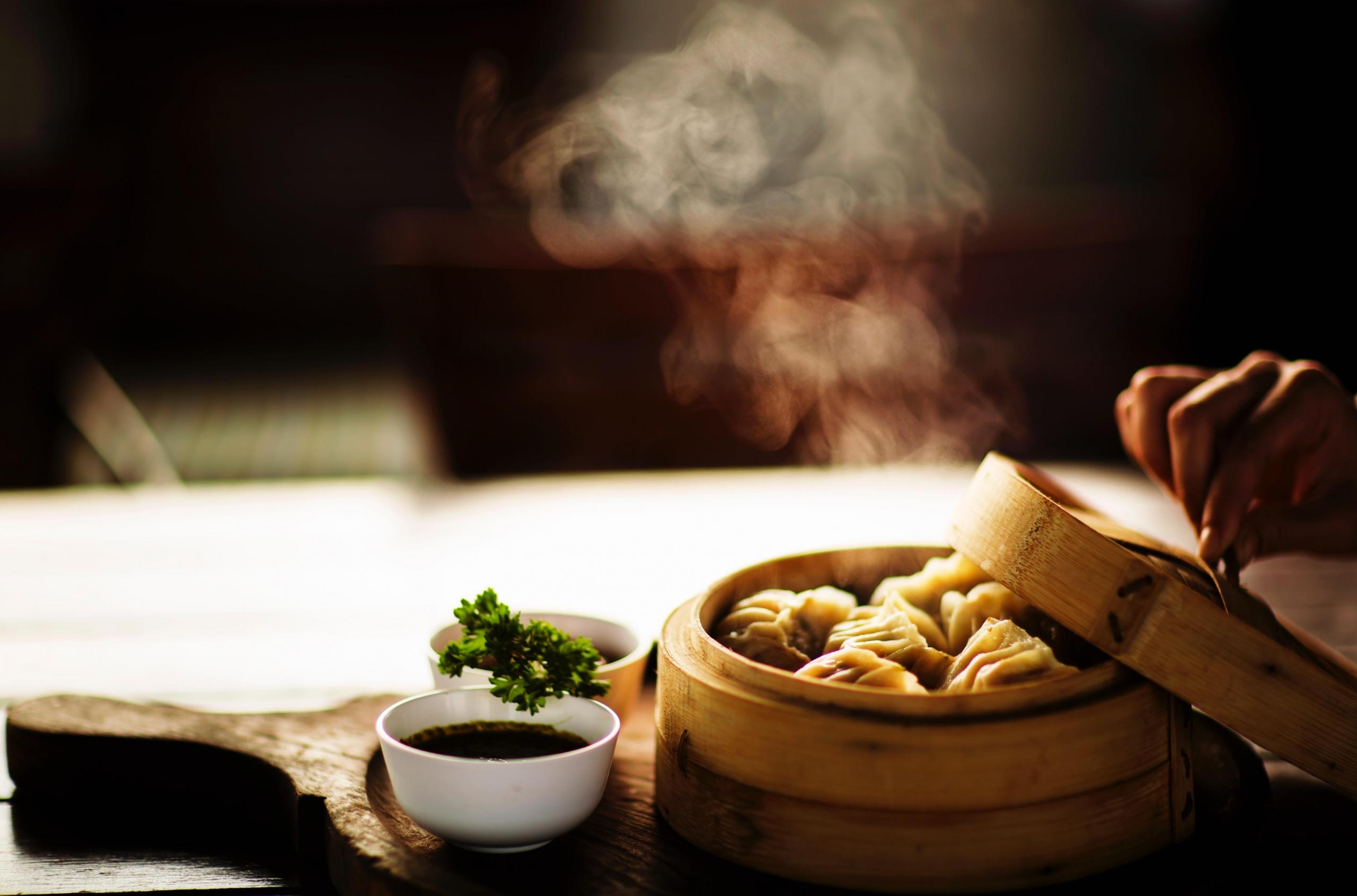 dumplings ligger i en steamer, en hånd løfter lokket av, og damp kommer ut og treffes av sollys