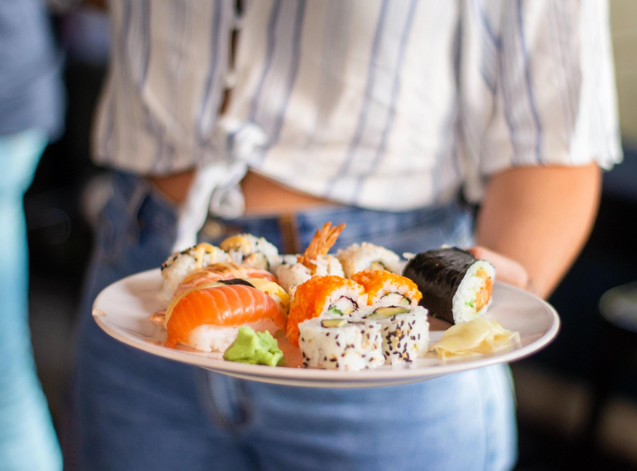 en person holder frem en tallerken med sushi, både maki og nigiri