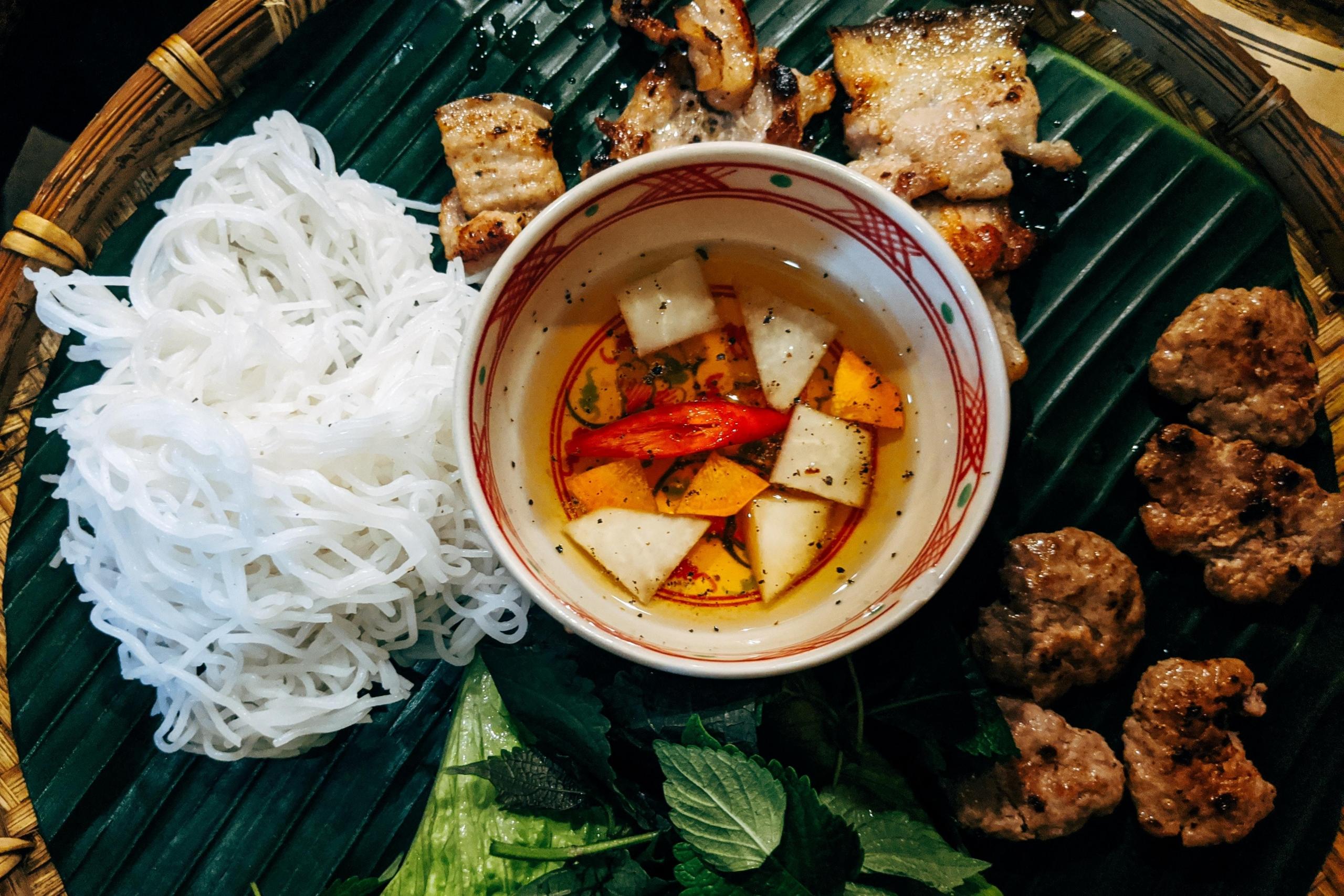 den vietnamesiske retten bun cha ovenfra. en skål med paprika og gulrot står midt på brettet, rundt ligger grillet kjøtt og nudler