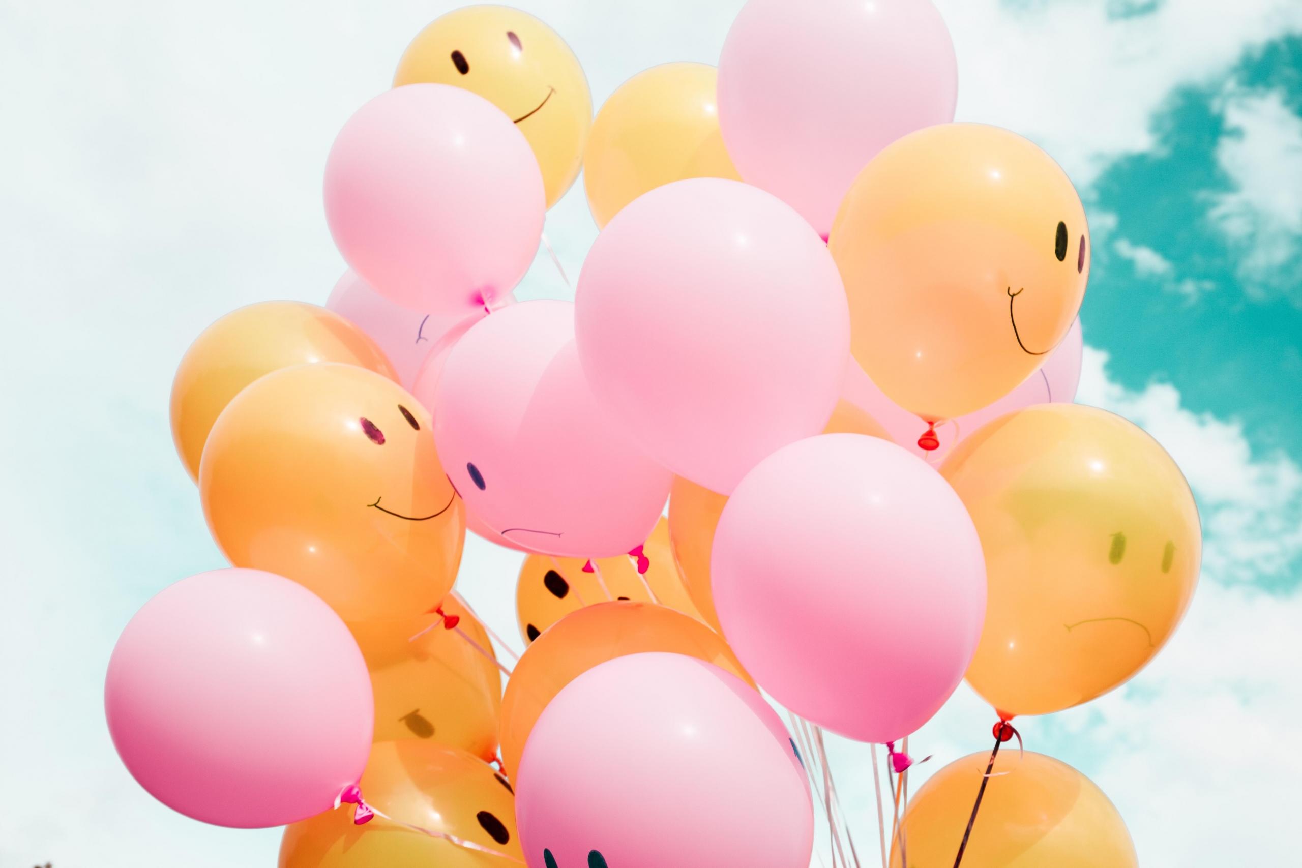 en klase ballonger med helium, halvparten er oransje og har smilefjes, resten er rosa og har trist fjes