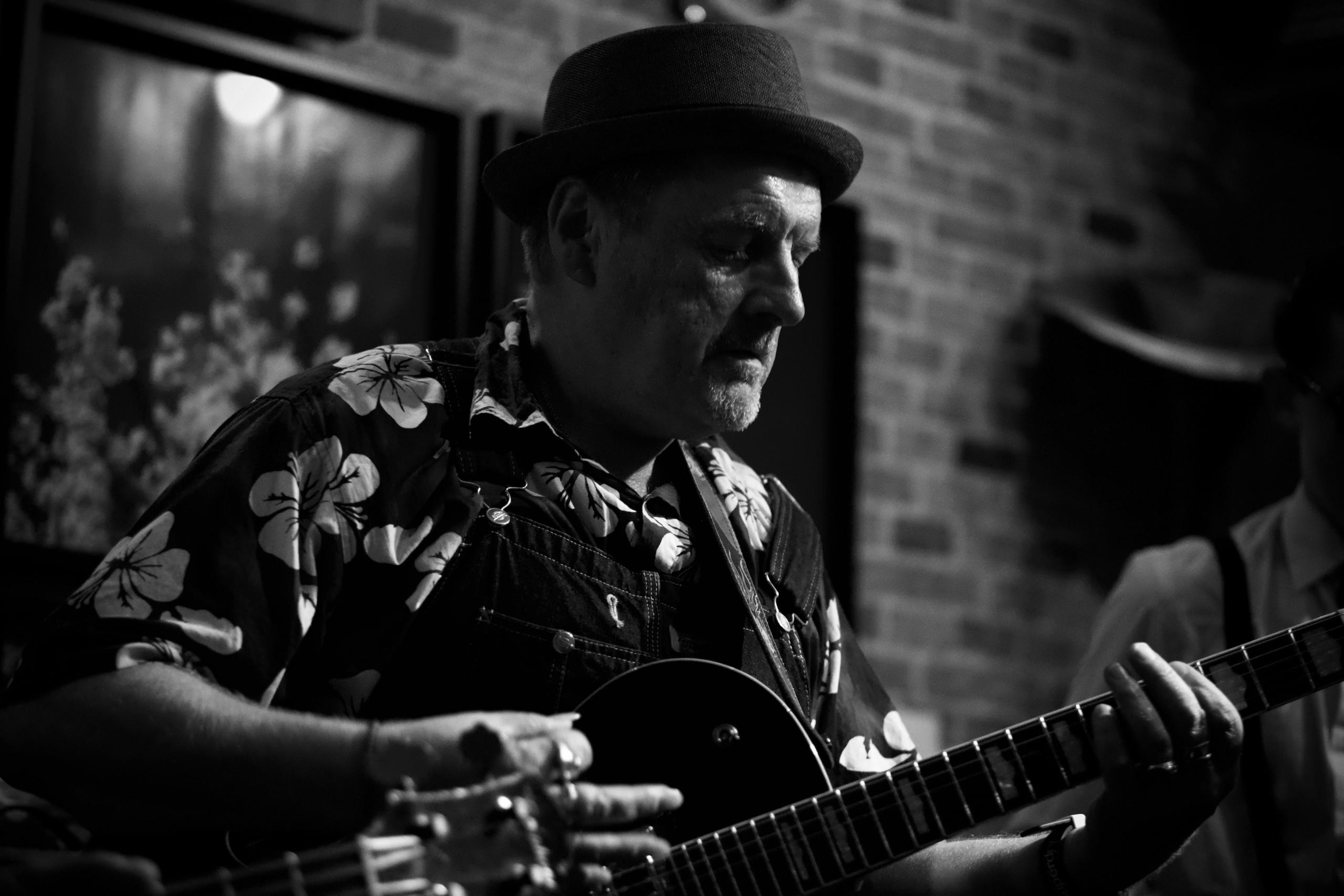 Eldre herre med hatt spiøller gitar.