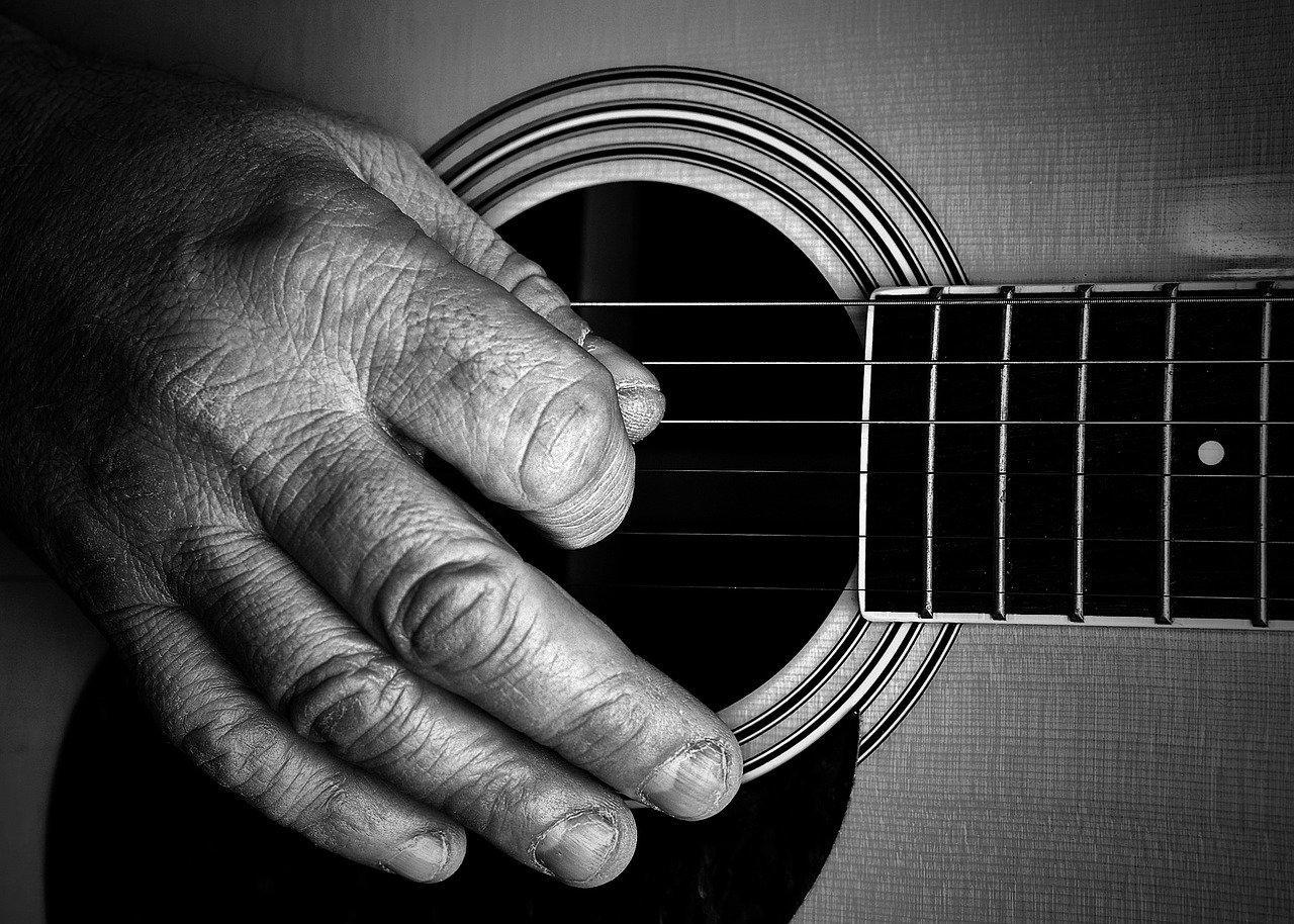 Hånda til en eldre person løper over gitarstrenger.
