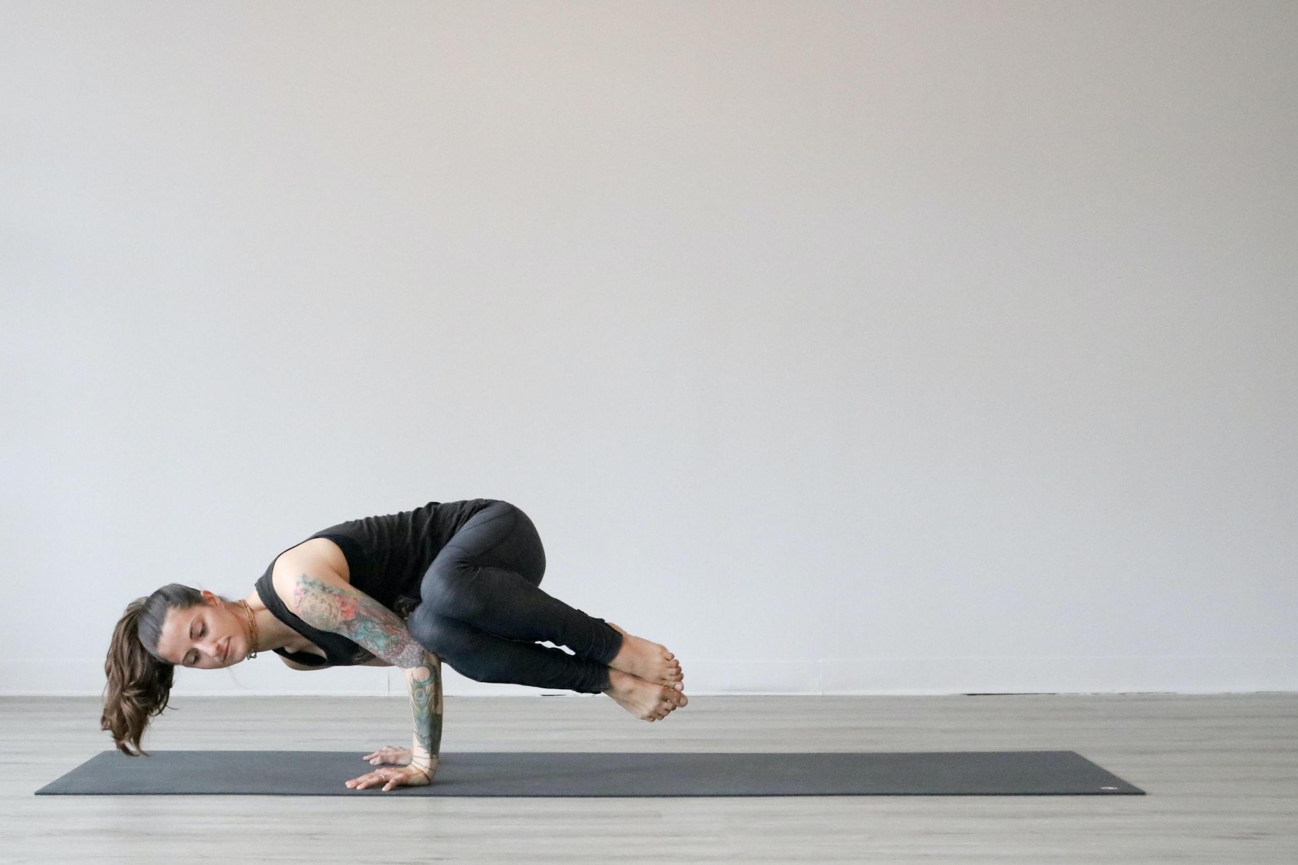 en kvinne står på hendene på en yogamatte, hun lener knærne på albuen og har vridd kroppen sidelengs